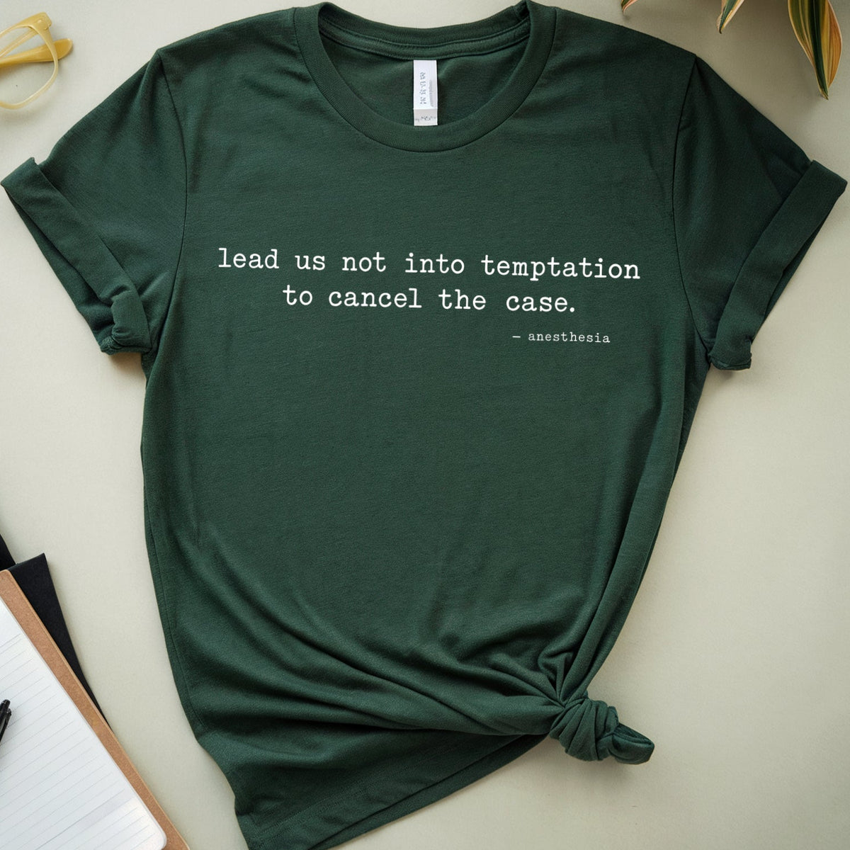 A dark forest green graphic t-shirt with a knotted hem, featuring the quote 'lead us not into temptation to cancel the case.' in white text.