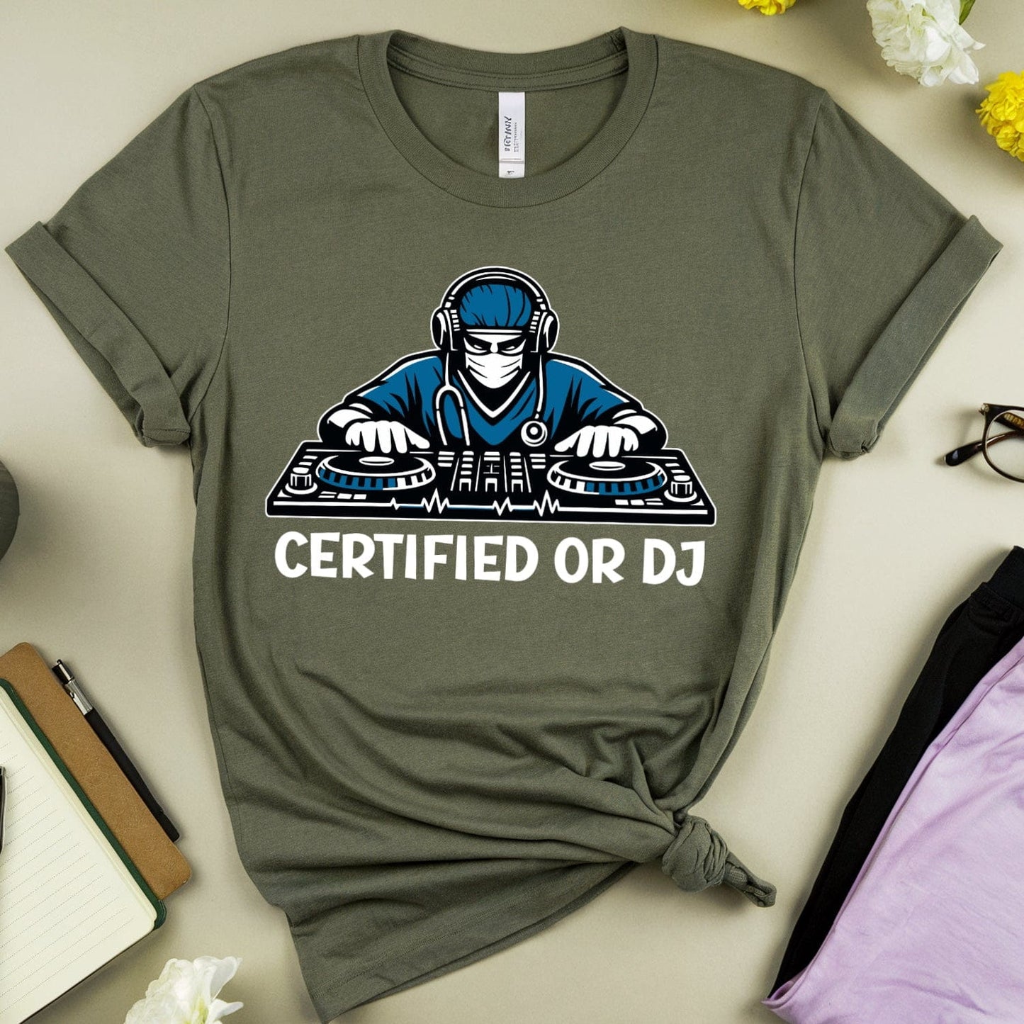 Green t-shirt with a 'Certified or DJ' graphic on a light surface with flowers and accessories.