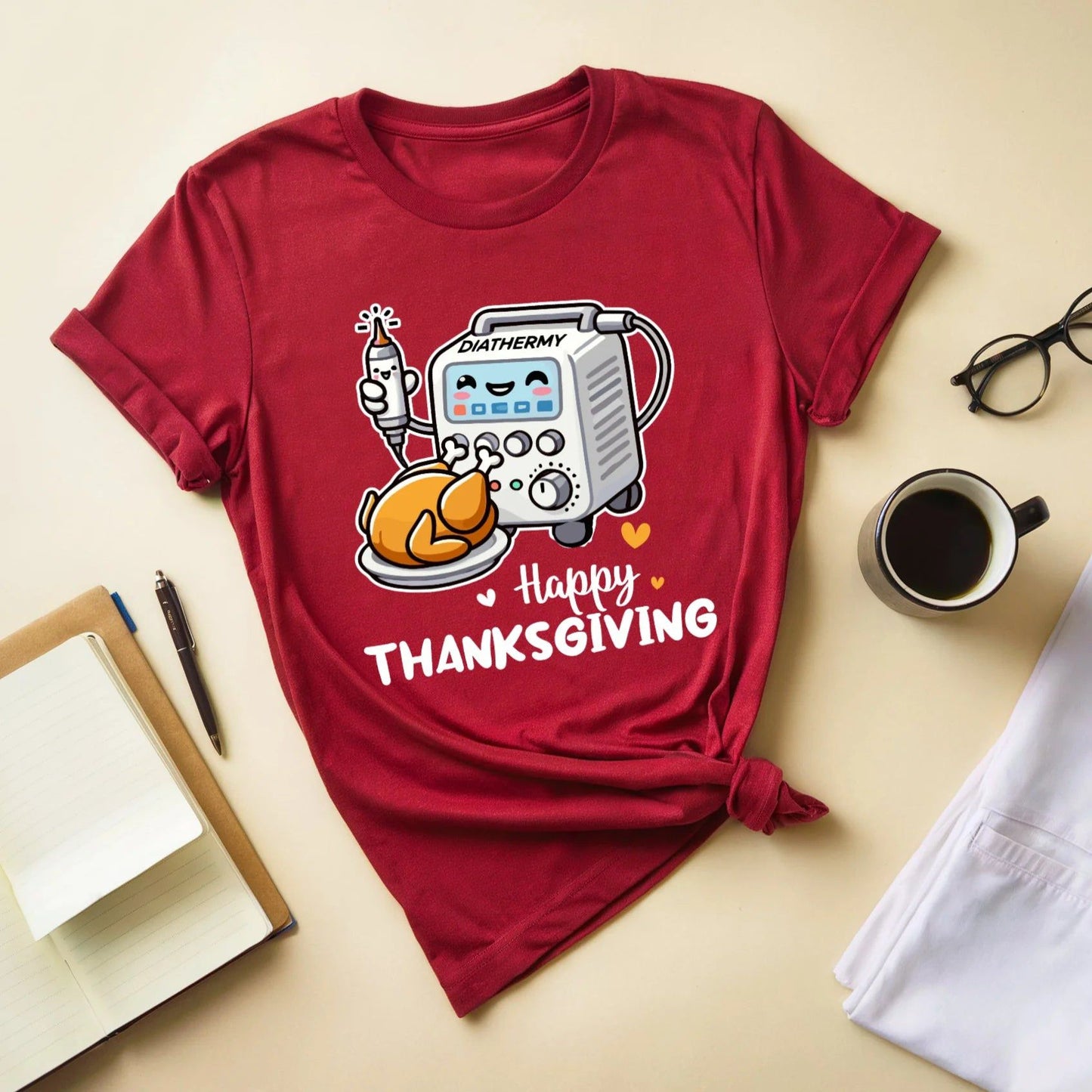 Red t-shirt with a Thanksgiving design for OR/Theatre crew on a beige surface with a cup, glasses, and notebook.