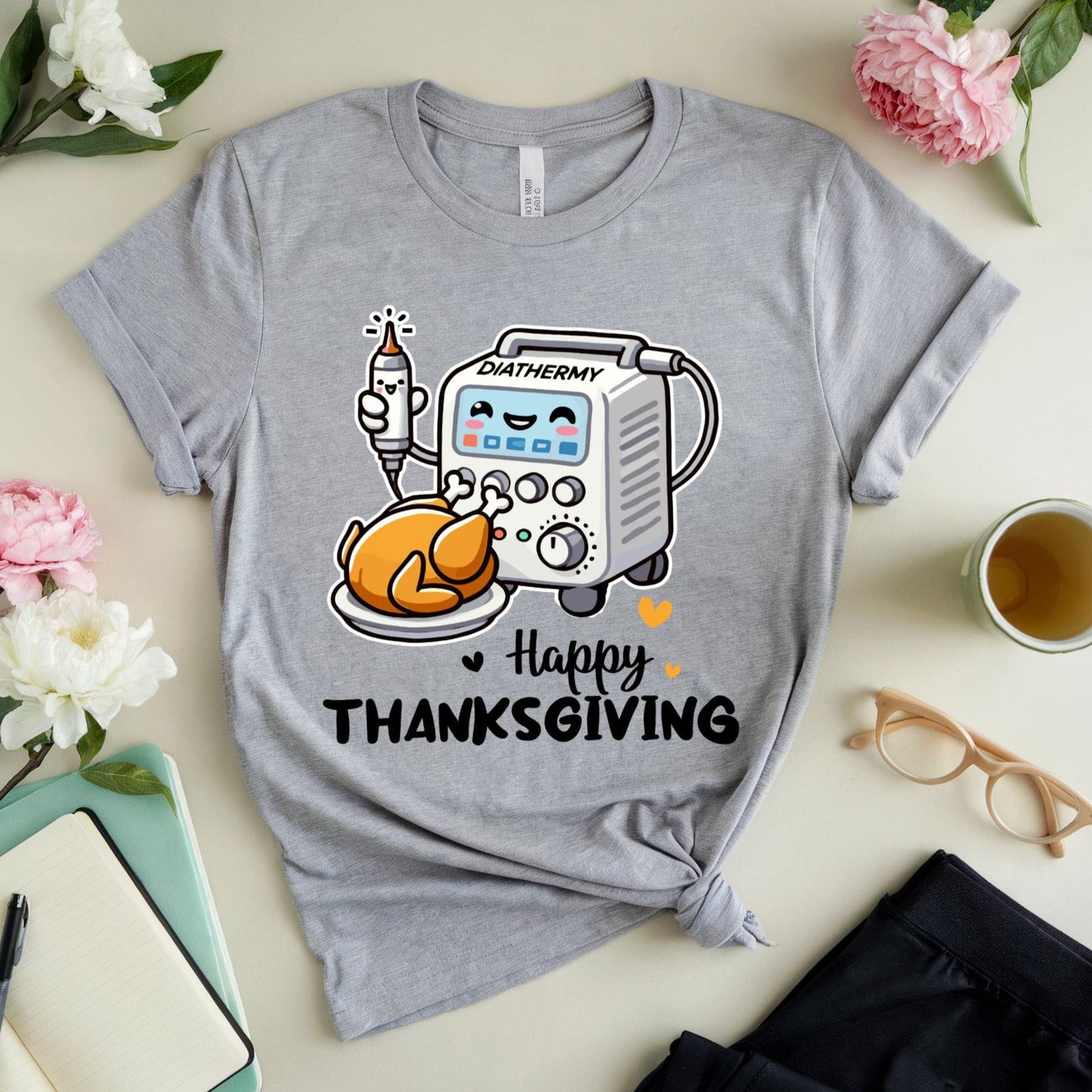 Gray t-shirt with cartoon graphic and 'Happy Thanksgiving' text for OR/Theatre crew on a light surface with flowers and a cup.