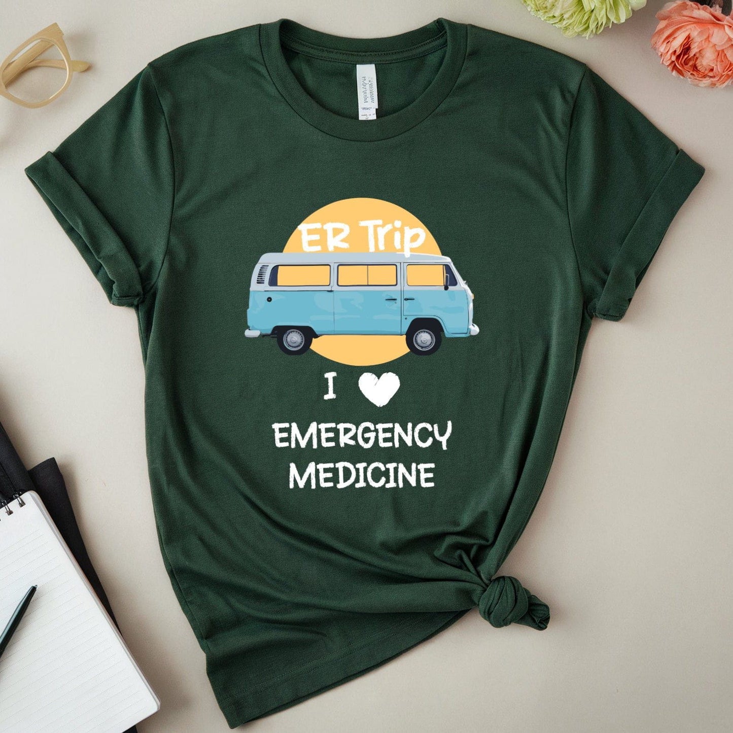 Green t-shirt with 'I love emergency medicine' design on a light surface with accessories.