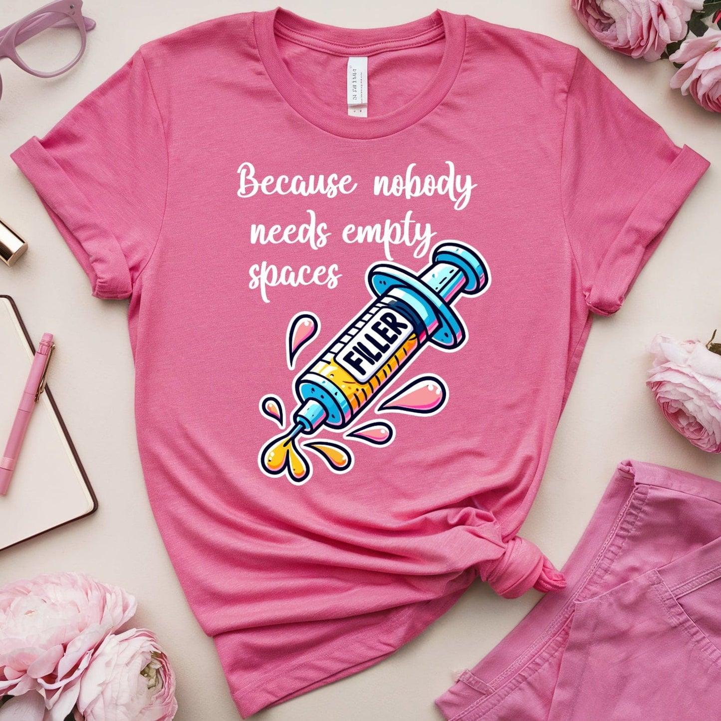 Pink t-shirt with colorful design and text, surrounded by pink accessories on a light background