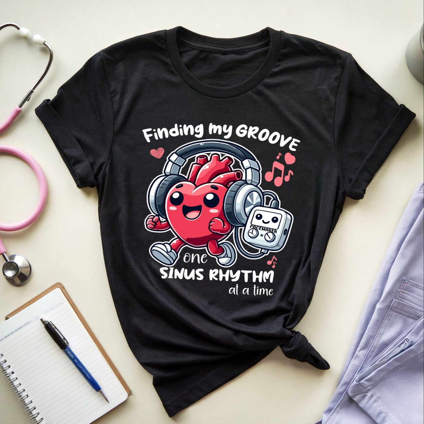Black t-shirt with a heart graphic and text for cardiologists on a light surface with medical equipment.