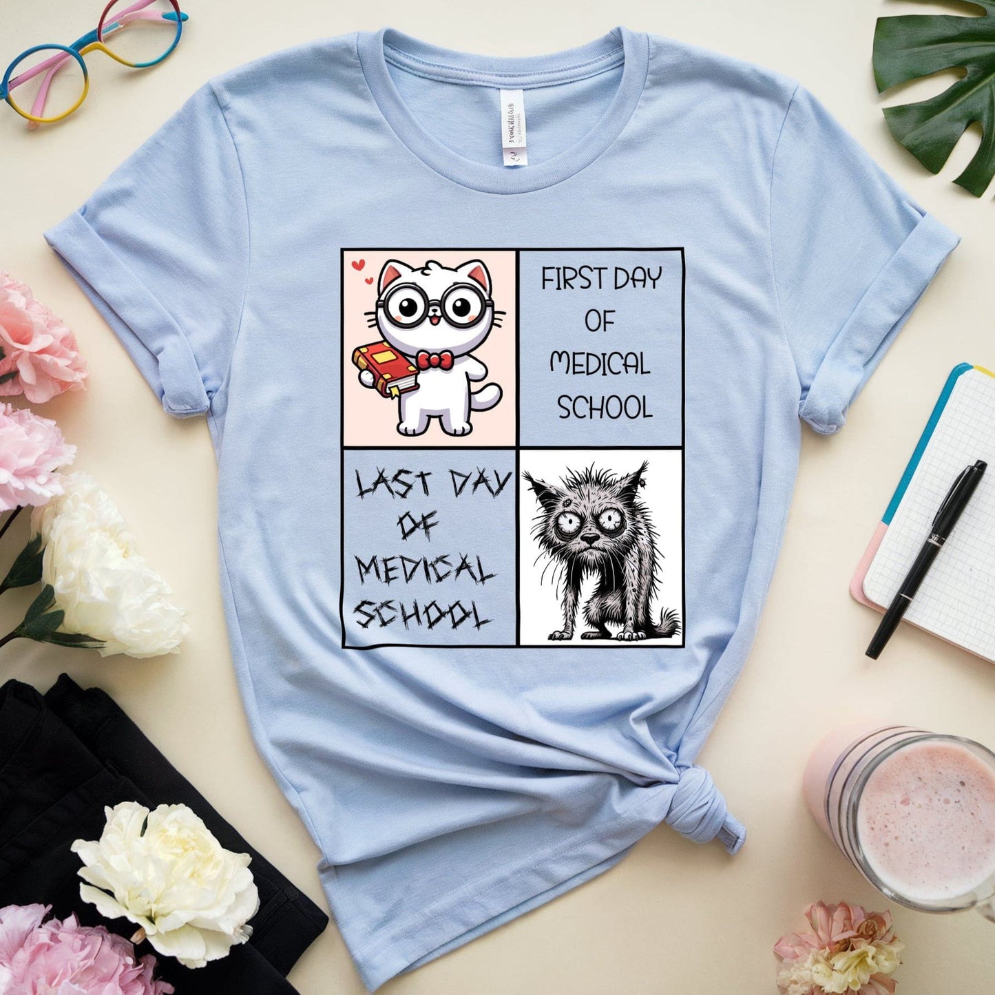 Light blue t-shirt with cartoon cat design on a table with flowers and stationery.