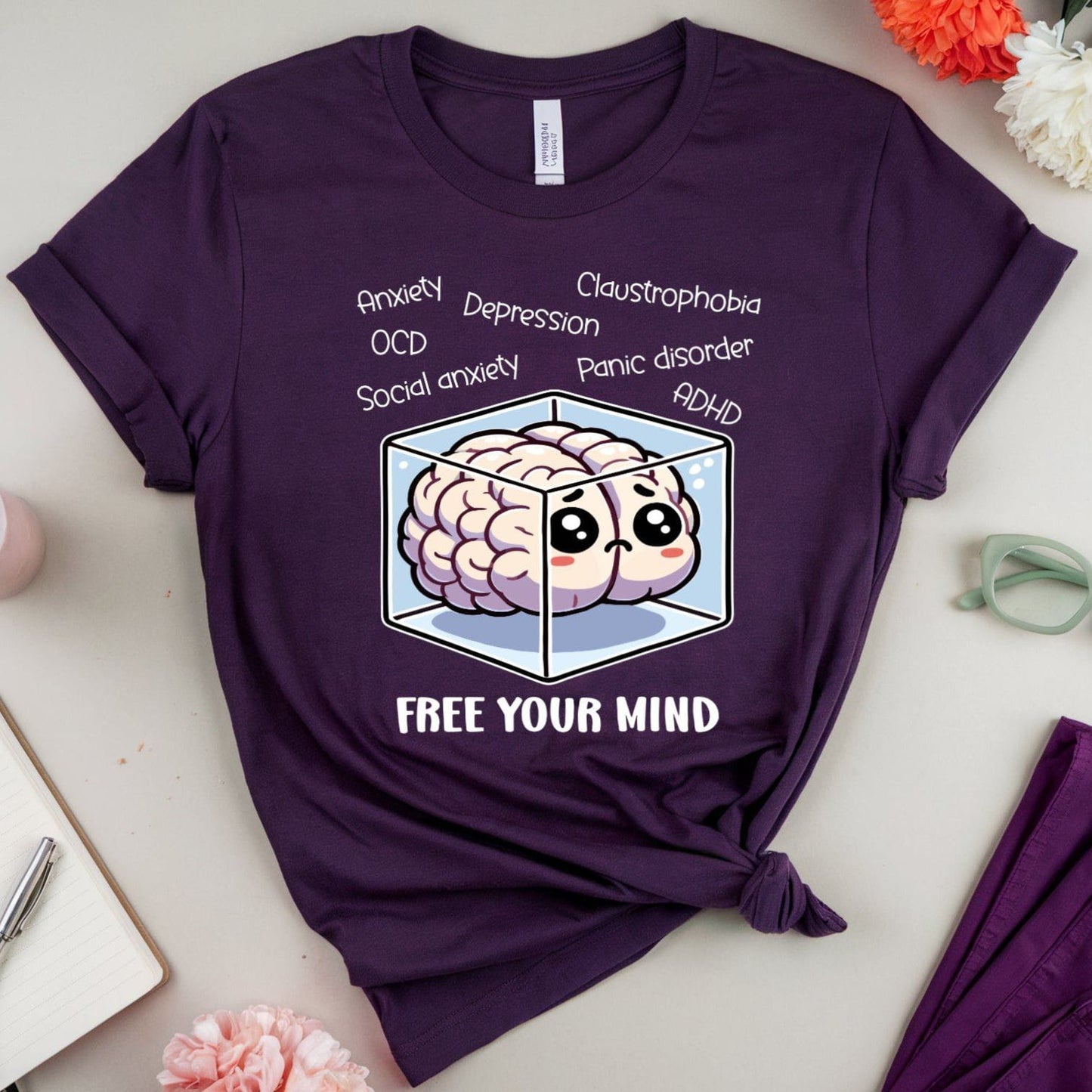 Purple t-shirt with brain graphic and text on a light surface with flowers and glasses.