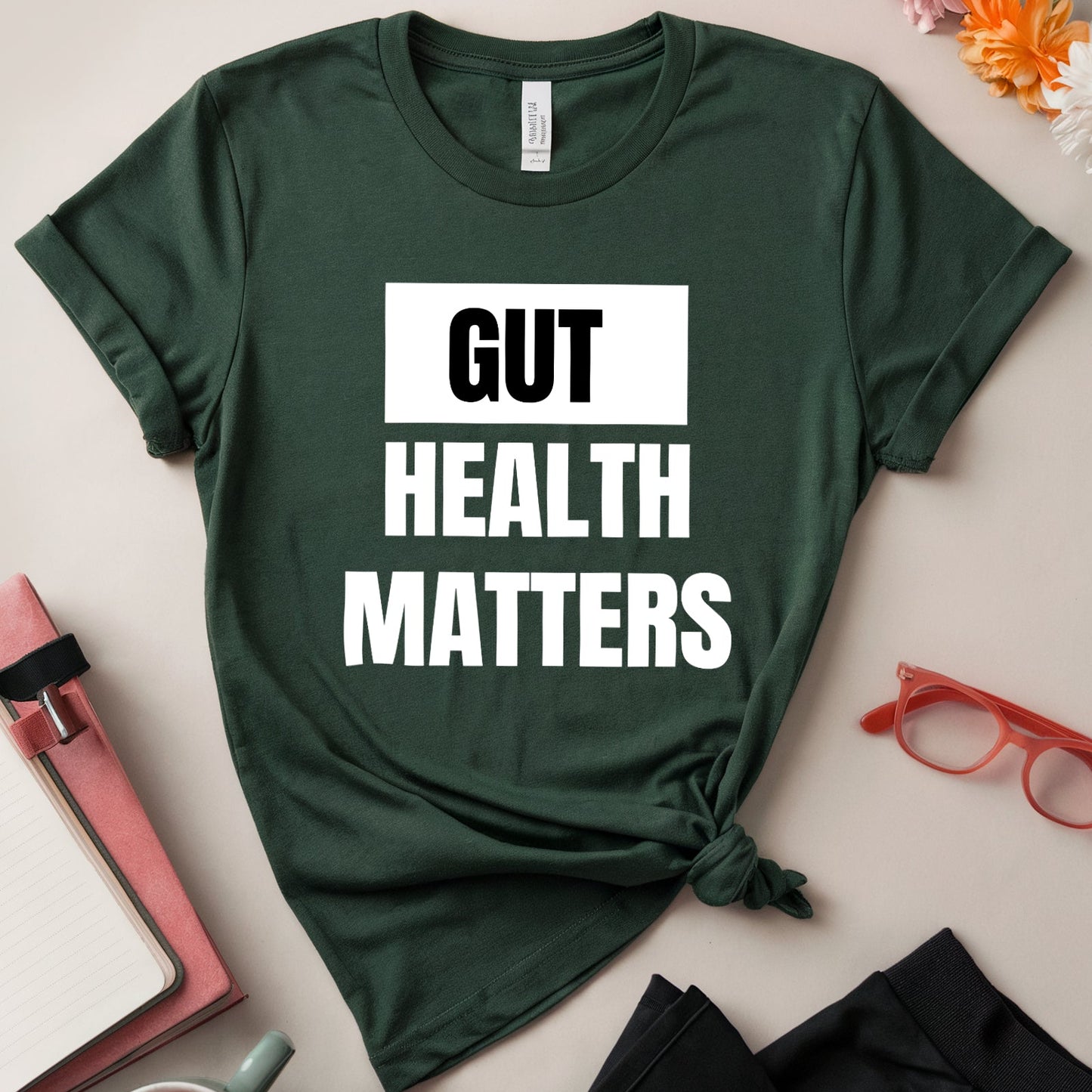 Green t-shirt with 'GUT HEALTH MATTERS' text on a light surface with accessories.