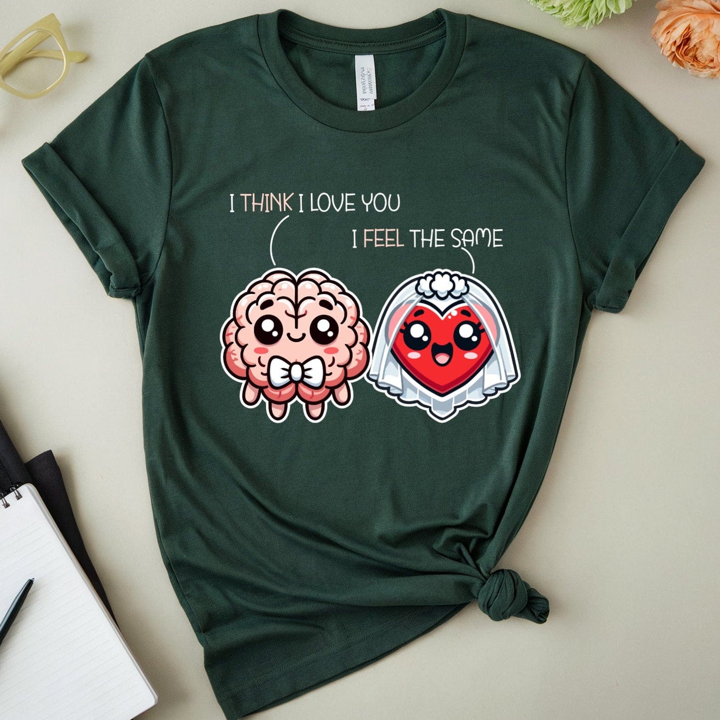 Green t-shirt with brain and heart design and text on a light surface with flowers and glasses.