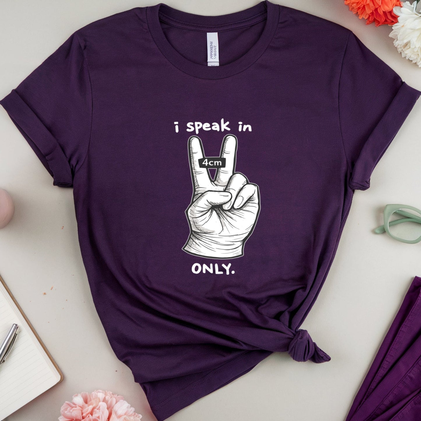 Purple t-shirt with a peace sign graphic and text on a light surface with flowers and glasses.
