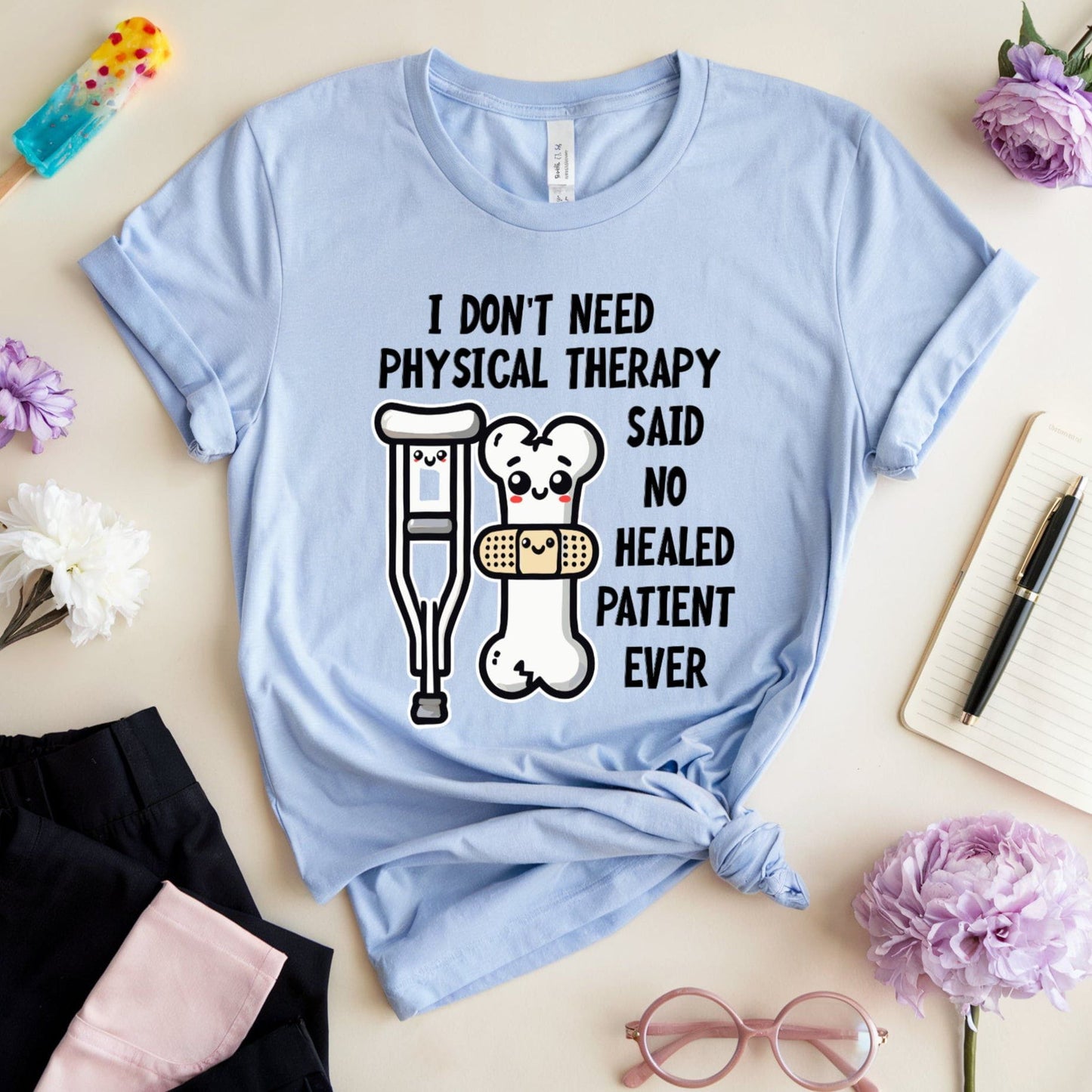 Light blue t-shirt for orthopedics with humorous graphic and text on a light surface with flowers and stationery.