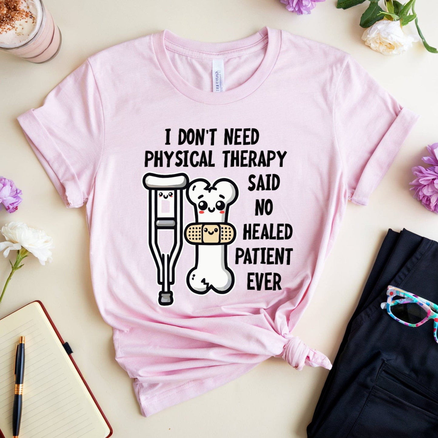 Pink t-shirt for orthopedics with humorous text and graphics on a light surface with flowers and a drink.
