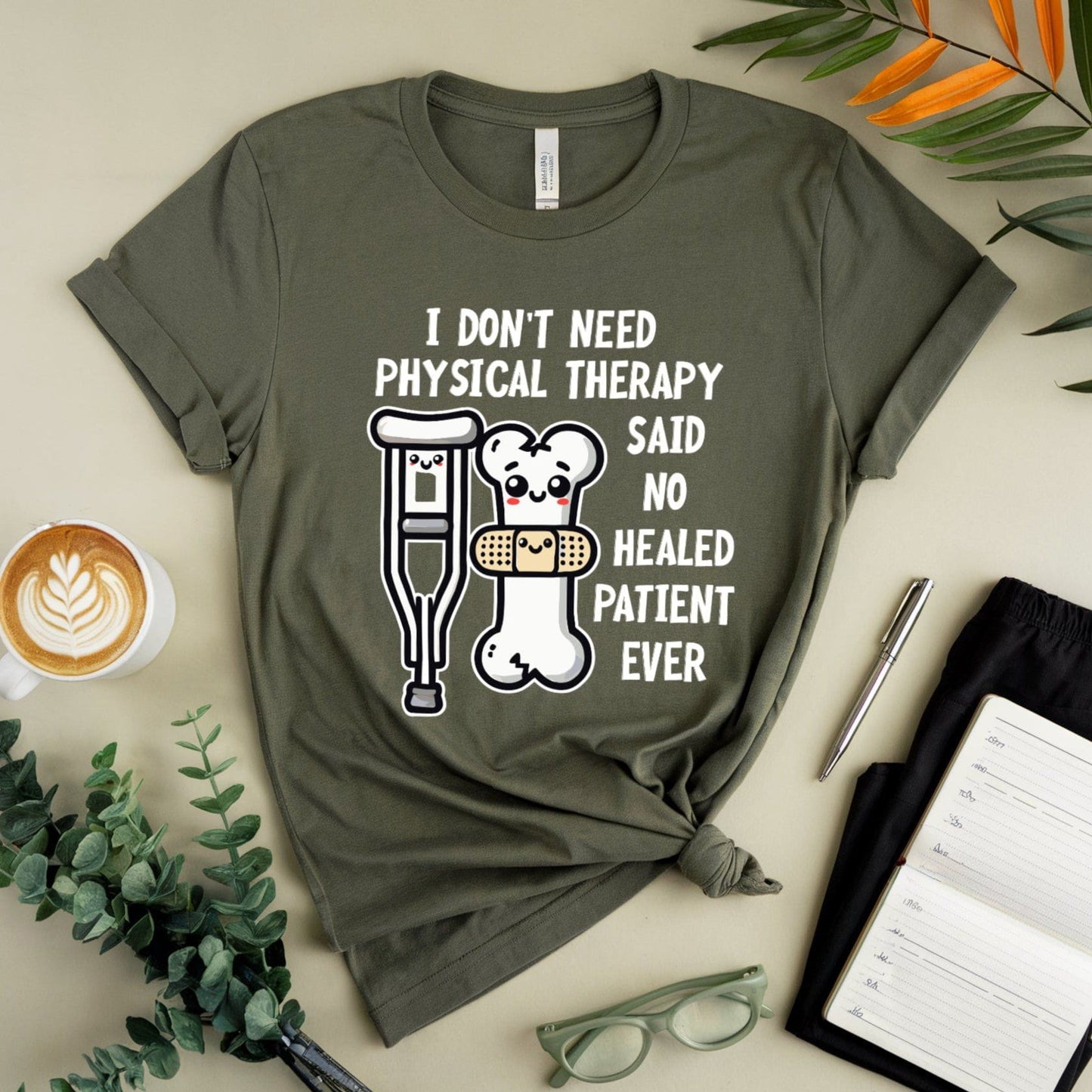 Military green t-shirt for orthopedics with humorous design and text on a light surface with coffee, glasses, and plants.