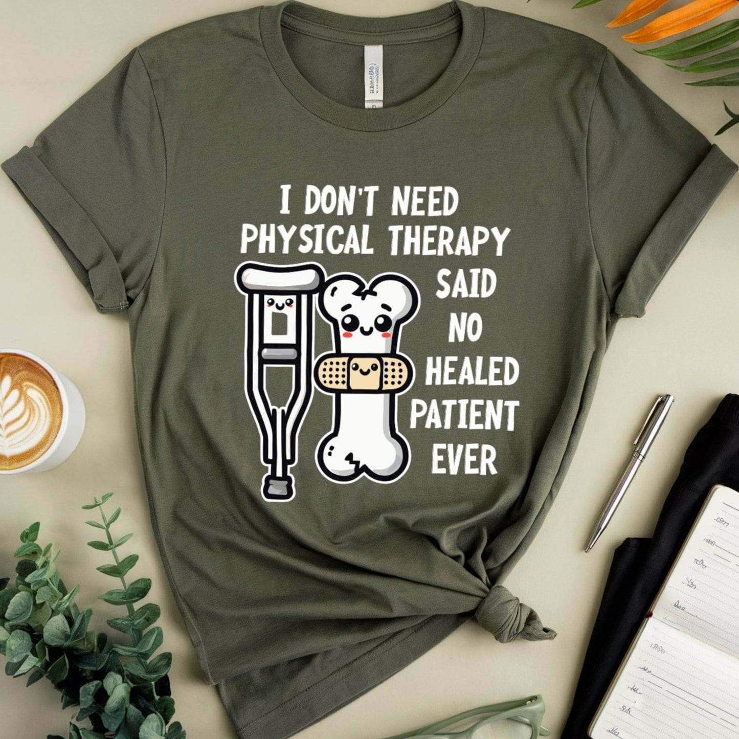 Military green t-shirt for orthopedics with humorous design and text on a light surface with coffee, glasses, and plants.
