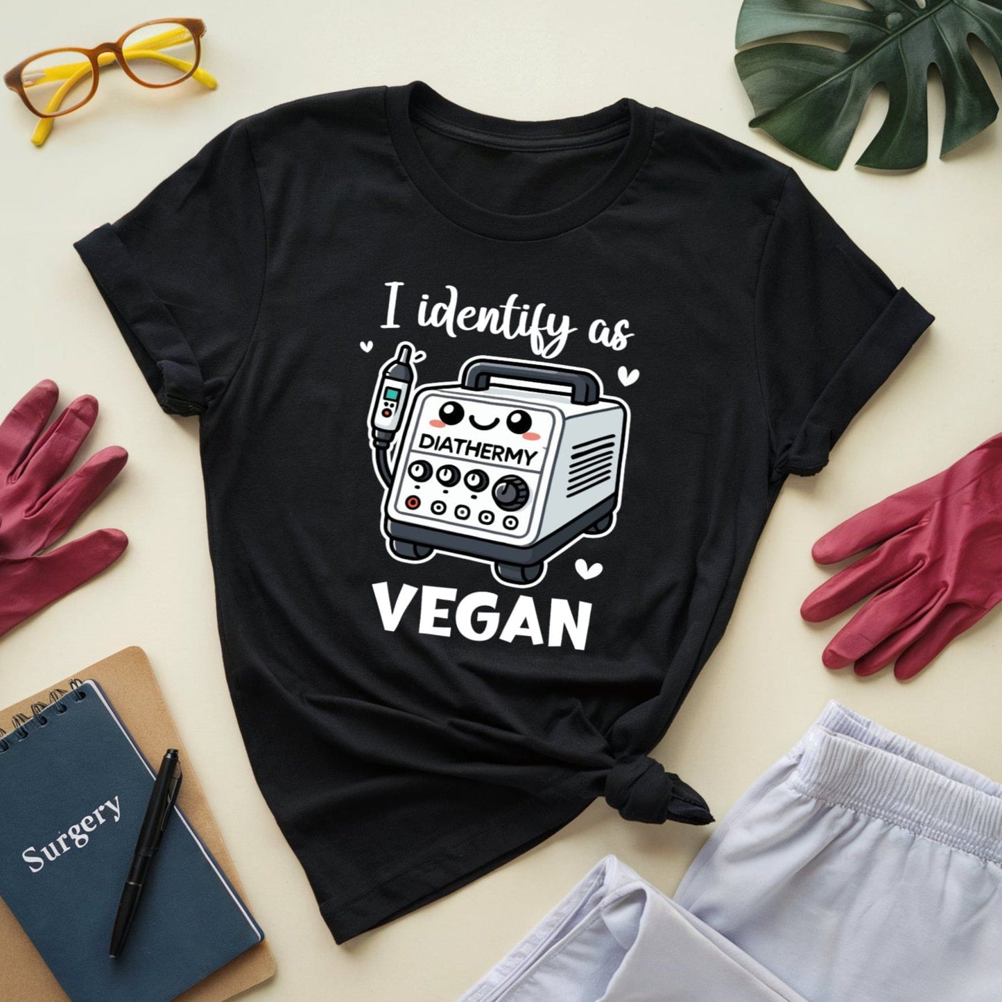 Black t-shirt with 'I identify as Vegan' graphic on a light surface with accessories.