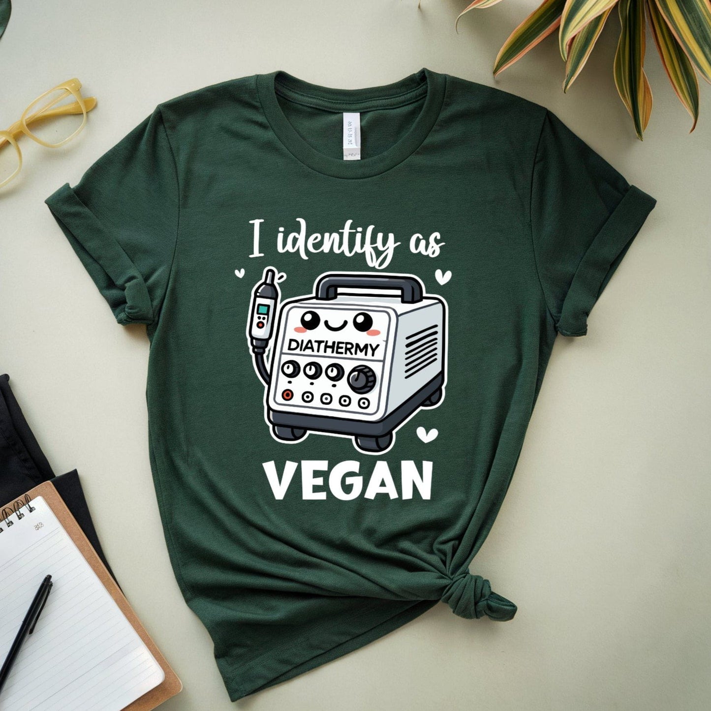 Green t-shirt with a graphic and text on a light surface with plants and stationery items.