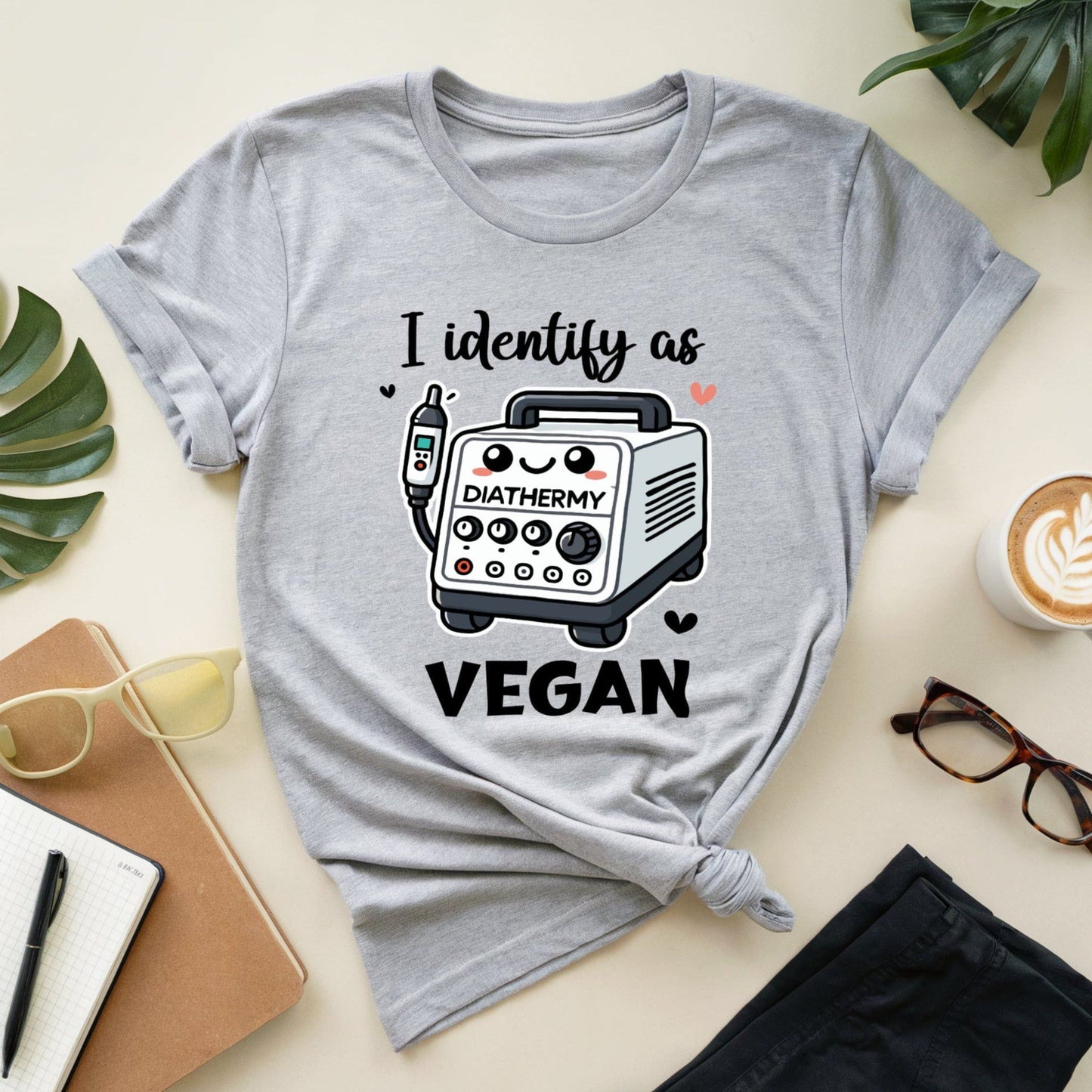Gray t-shirt with a graphic and text 'I identify as DIATHERMY VEGAN' on a light surface with accessories.