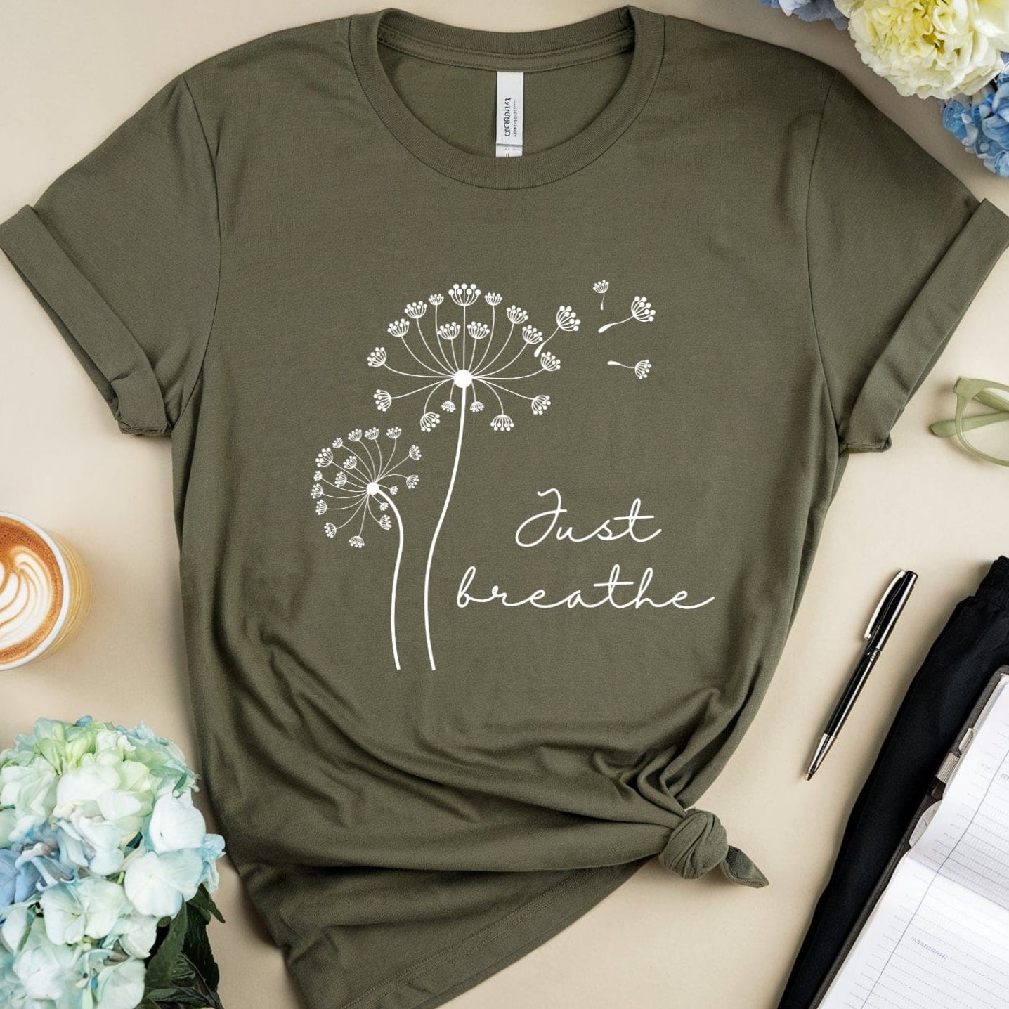 Green t-shirt with 'Just breathe' design on a table with flowers and a coffee cup.