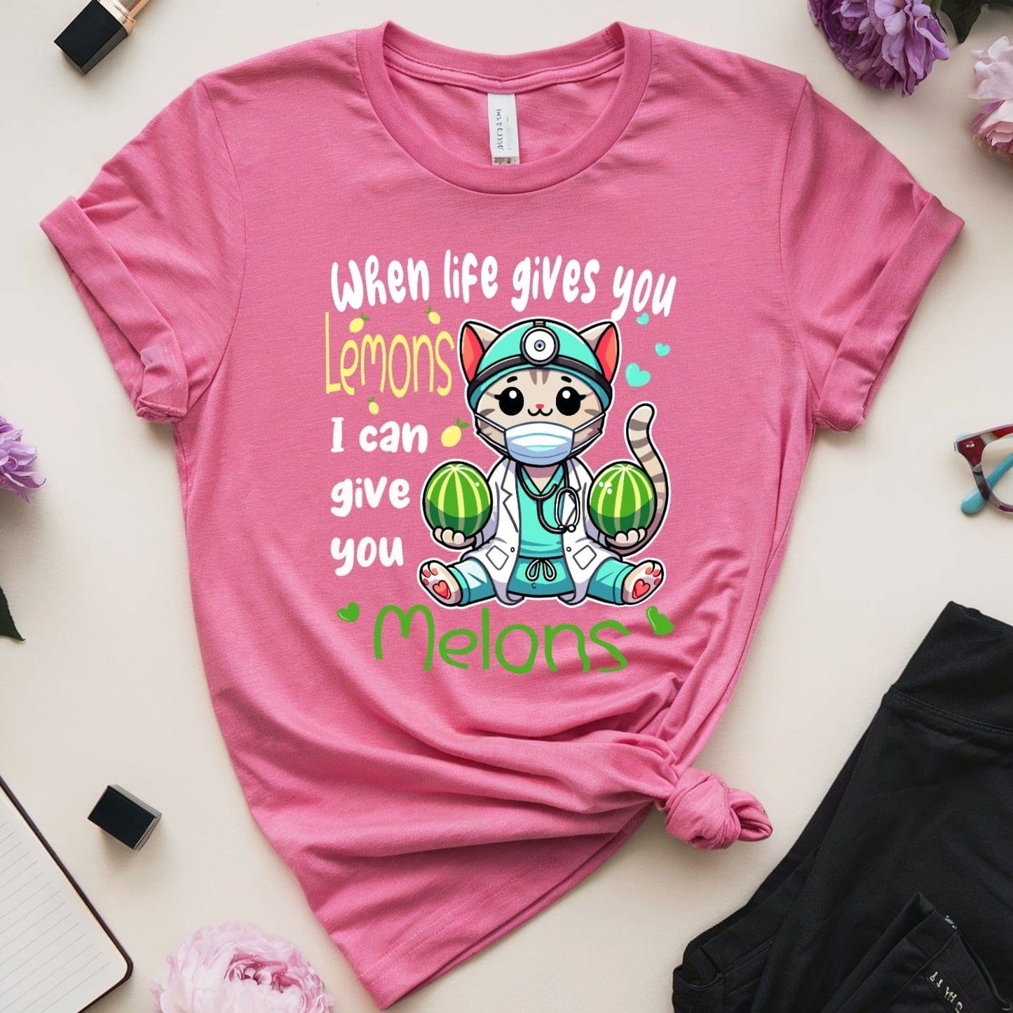 Pink t-shirt with a cartoon character and text on a white surface with flowers and accessories.