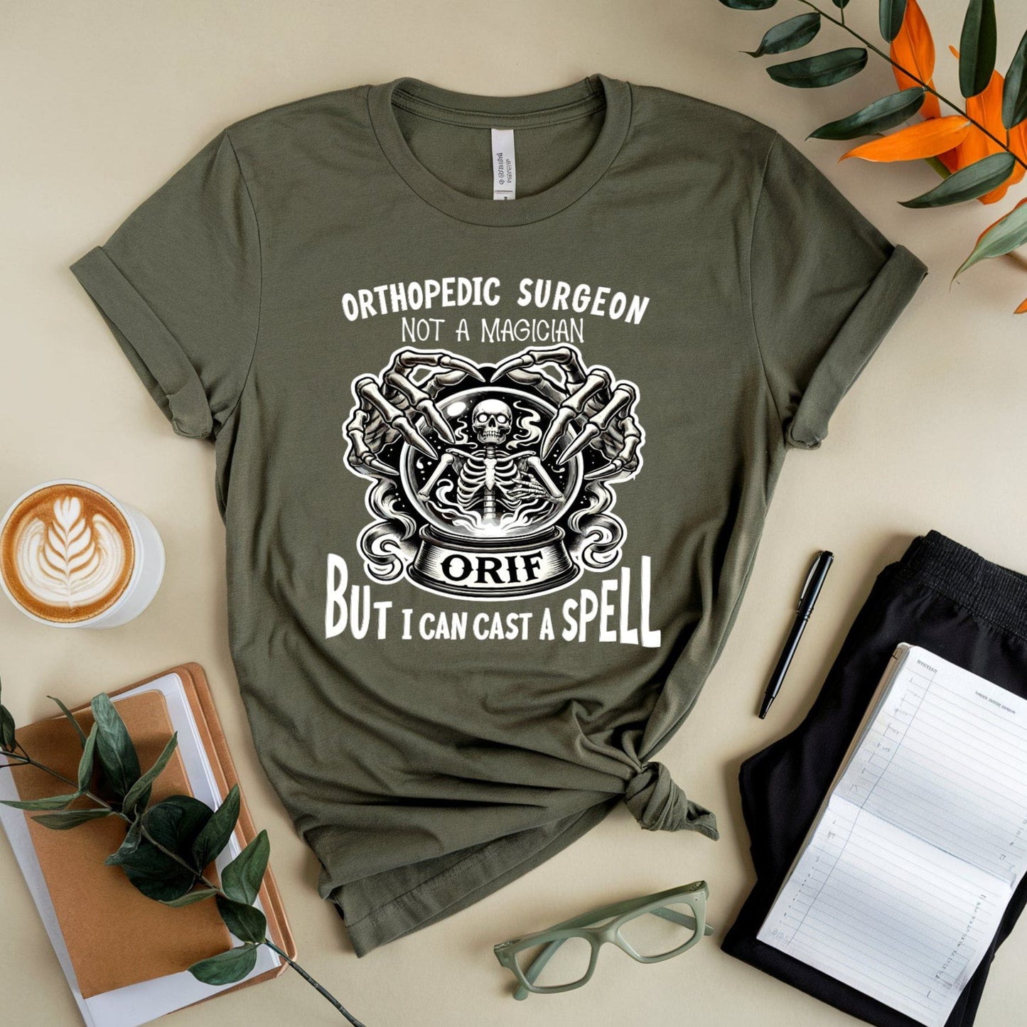 Green t-shirt with printed design and text on a beige surface with a cup of coffee, notebook, and glasses.