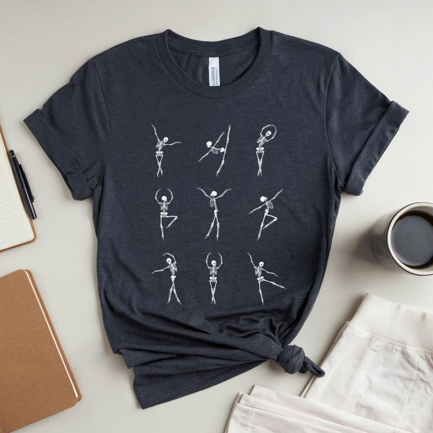 Navy t-shirt with skeleton ballerina designs for orthopedics on a light surface with notebooks and a mug.