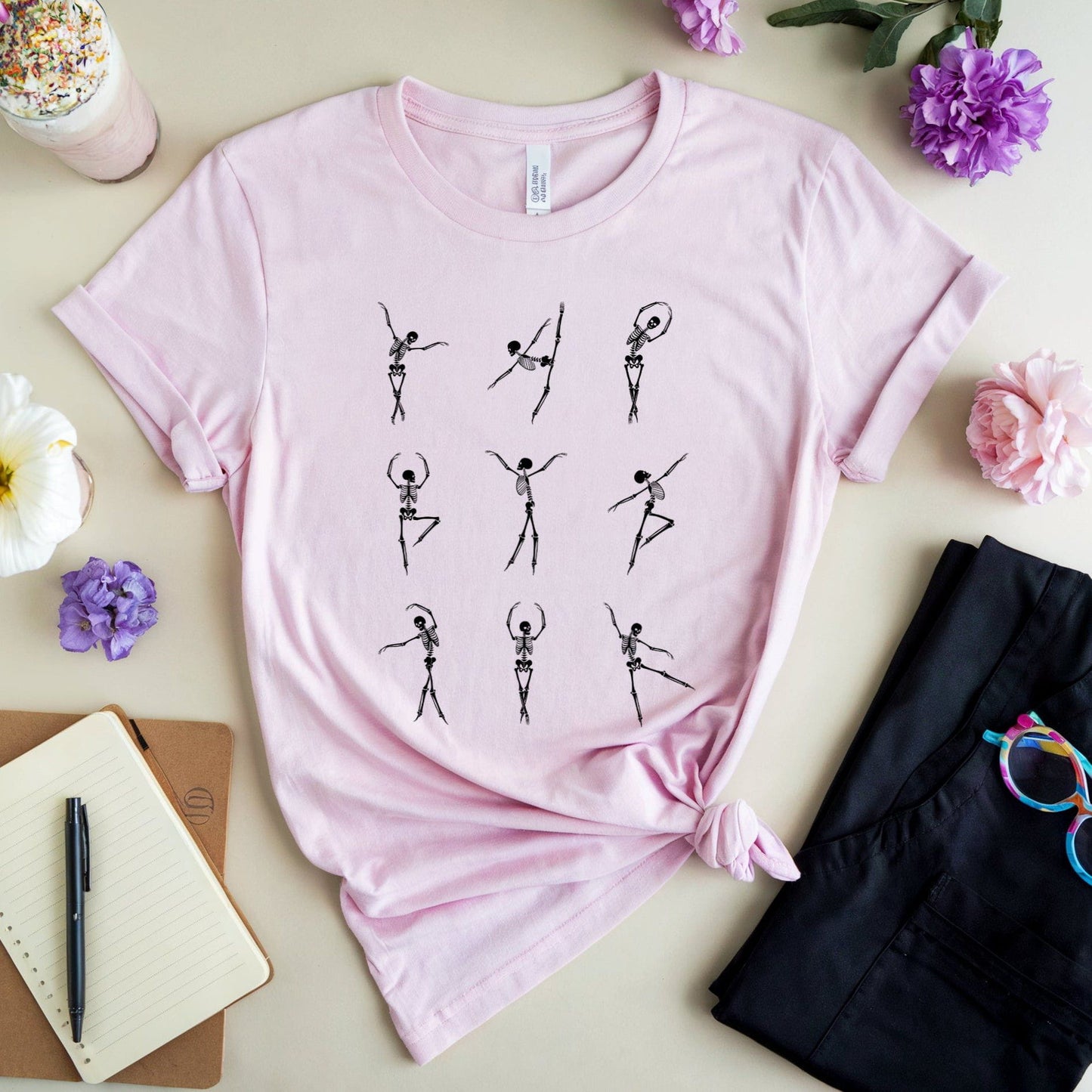 Pink t-shirt with skeleton dancer design for orthopedics on a table with flowers and a drink.