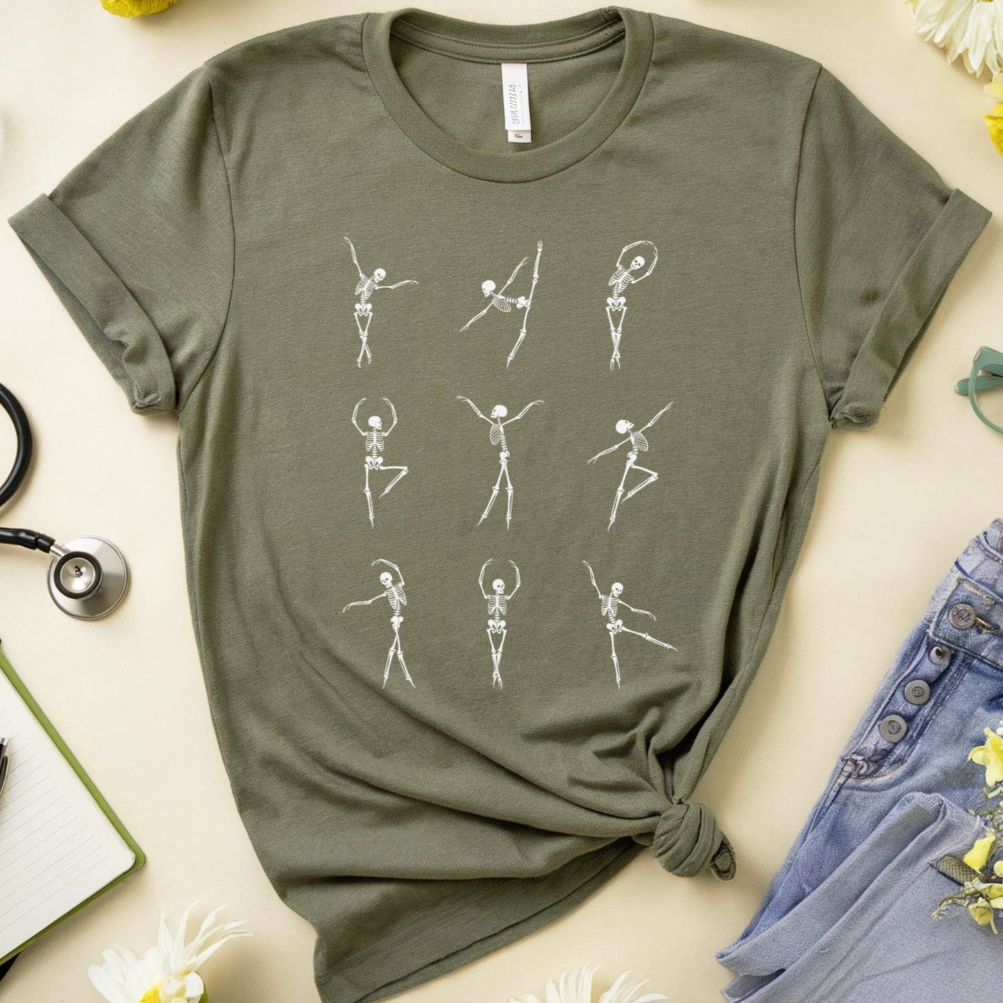 Green t-shirt with skeleton designs for orthopedics on a light surface with flowers and jeans.