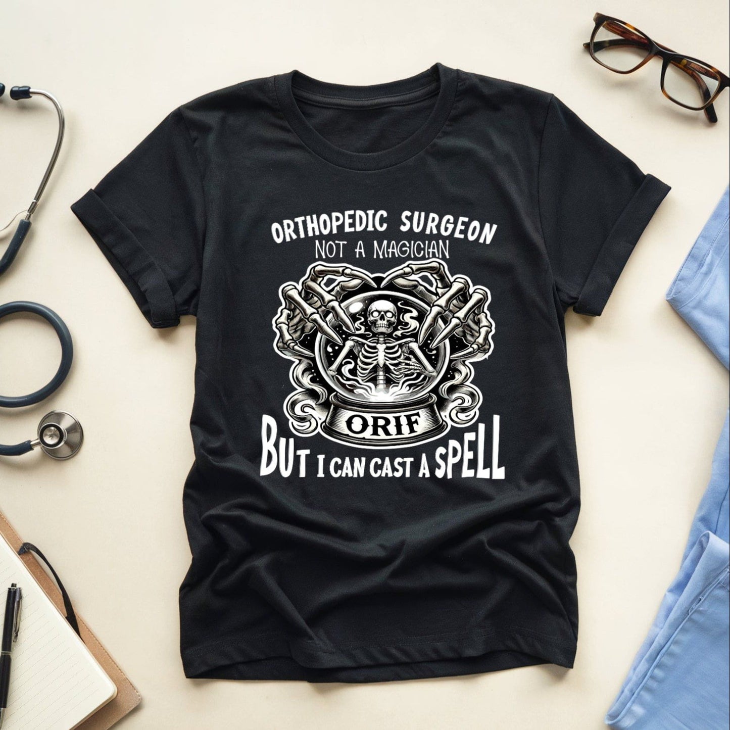Black t-shirt with orthopedic surgeon graphic and text on a light surface with medical items.