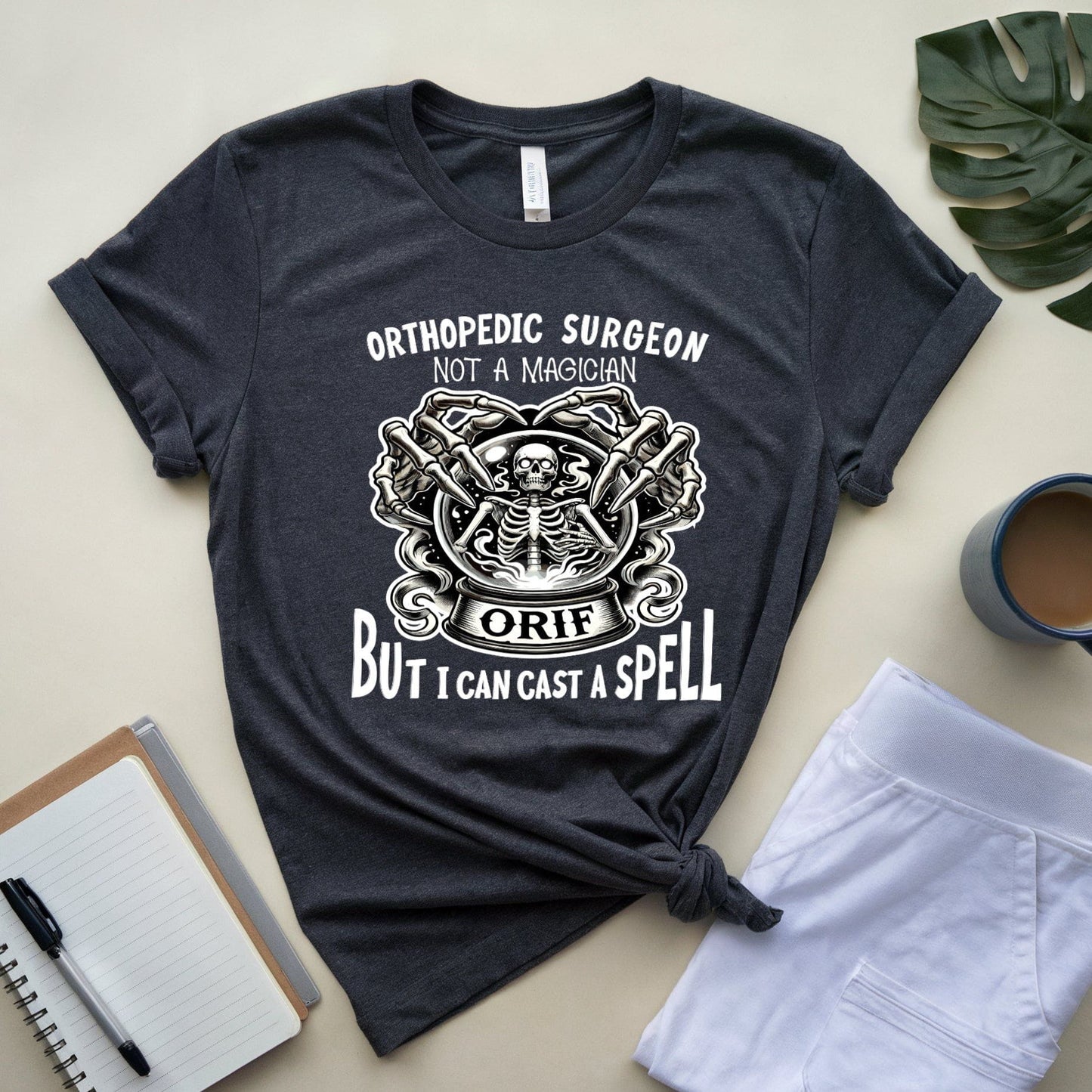 Dark gray t-shirt for orthopedic residents with humorous text design on a light surface with accessories.