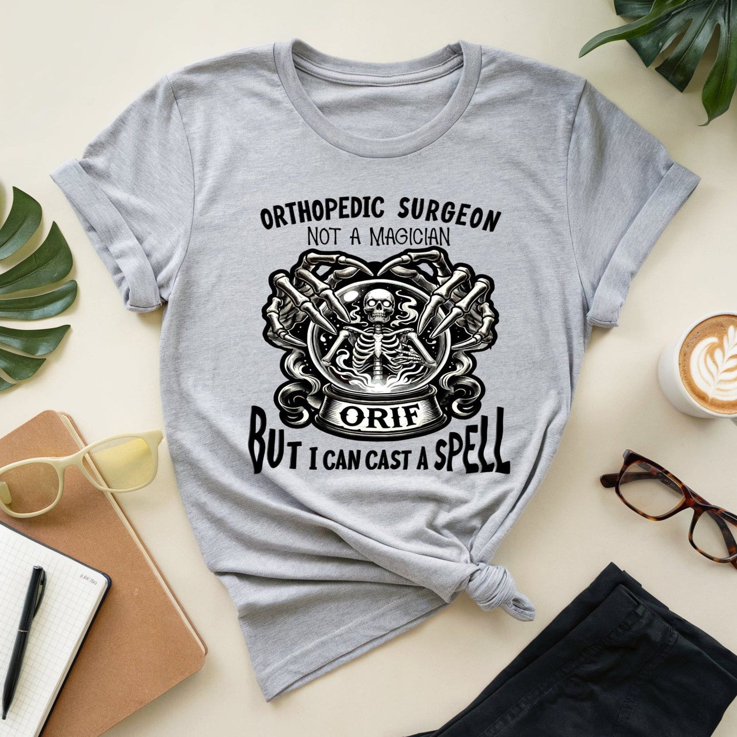 Gray t-shirt with orthopedic surgeon graphic and text on a light surface with accessories.