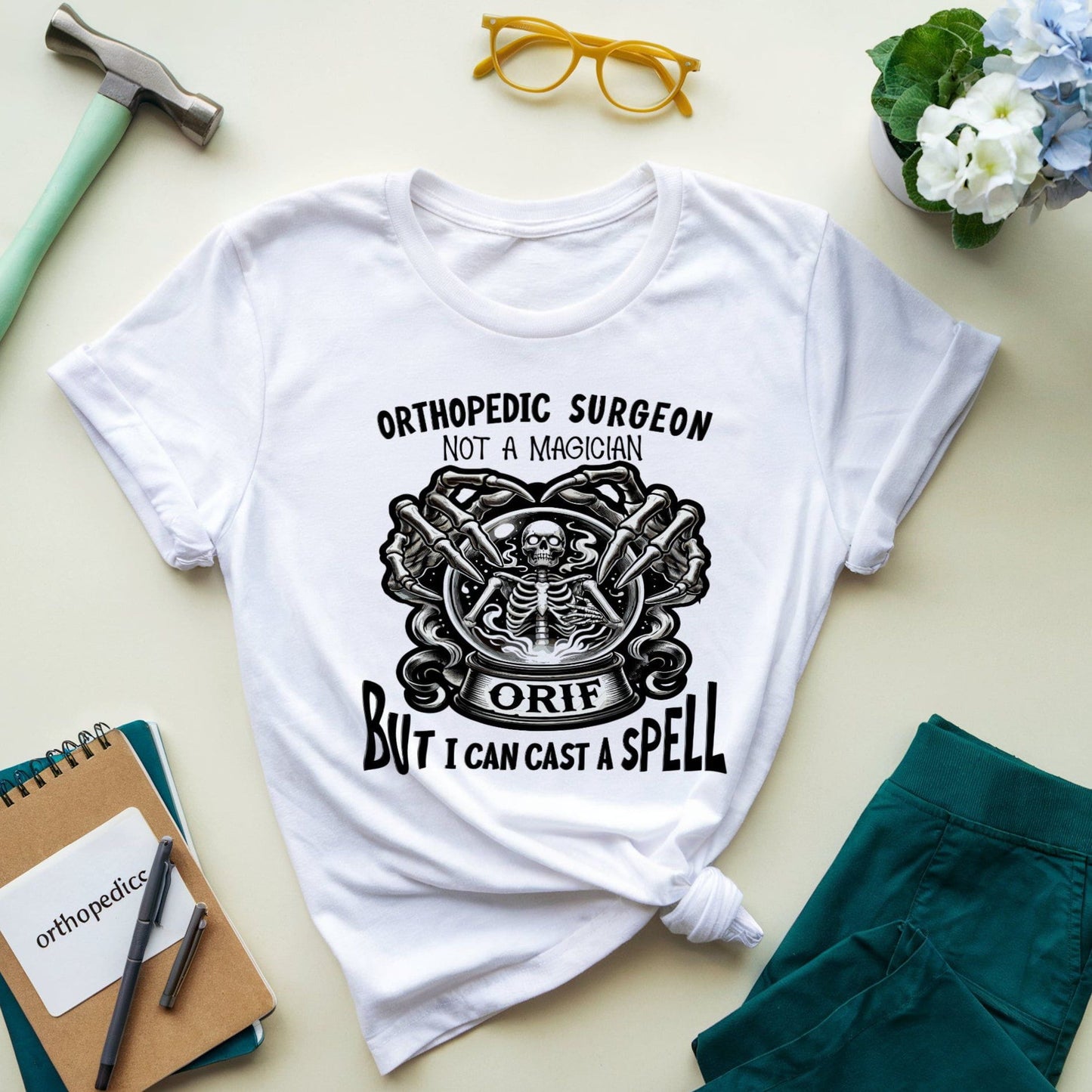 White t-shirt with graphic design and text for orthopedic surgeons on a light surface with accessories.