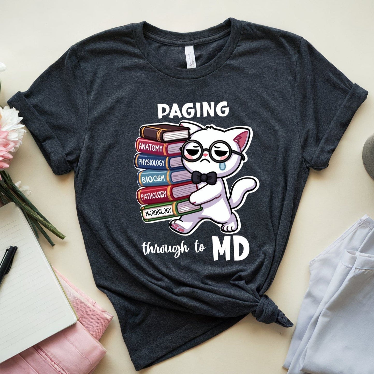 Black t-shirt with a cat graphic and text 'Paging through to MD' on a light surface with accessories.