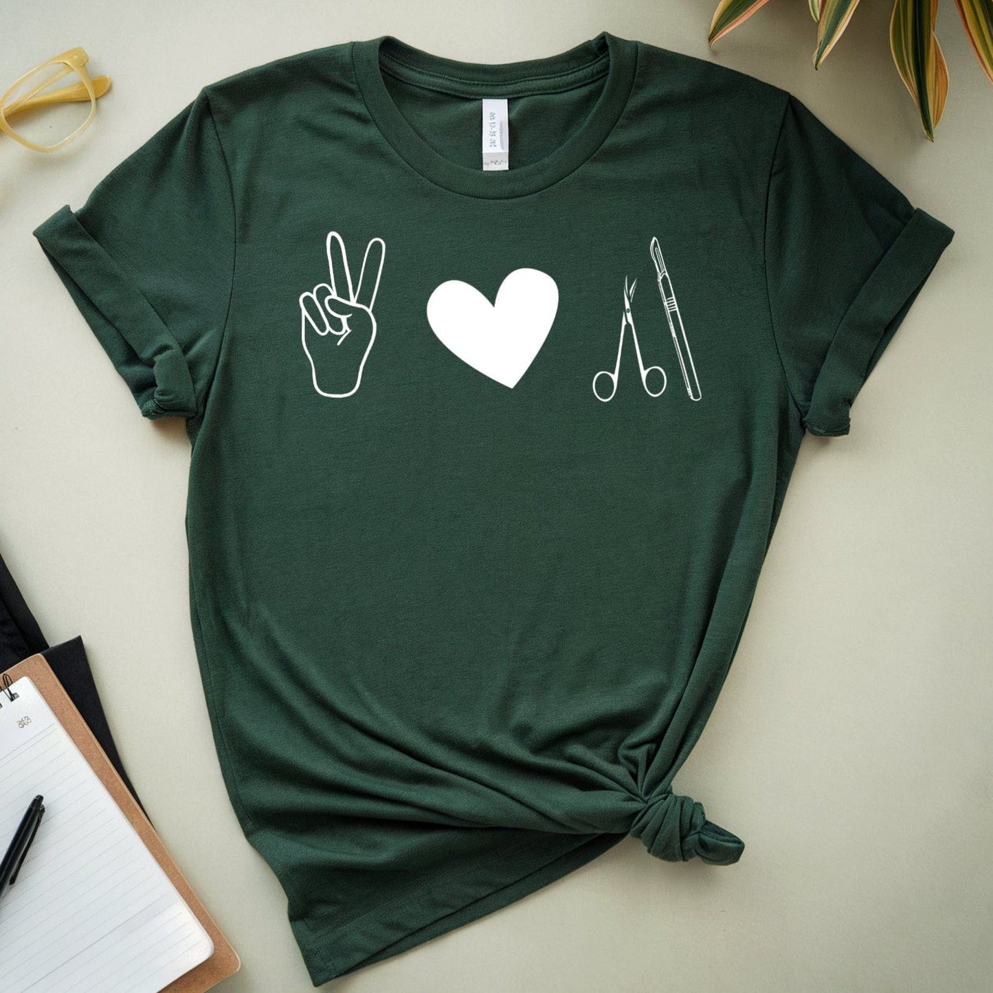 Green t-shirt for surgeons with symbols on a light surface with plants and stationery items.