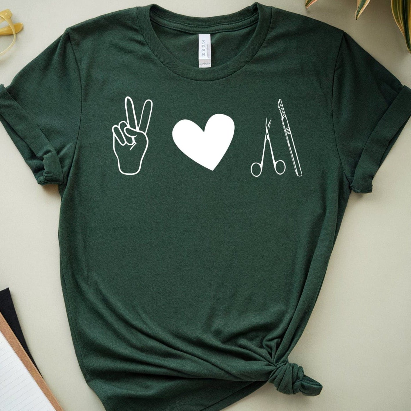 Green t-shirt for surgeons with symbols on a light surface with plants and stationery items.