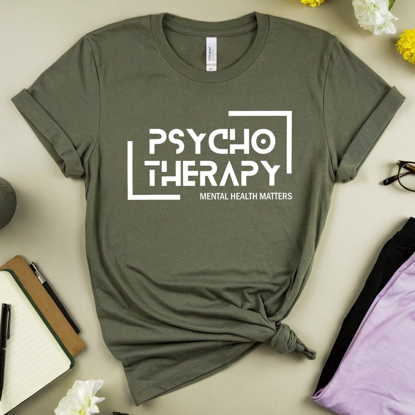Green t-shirt with 'Psychotherapy' text on a light surface with flowers and a mug.