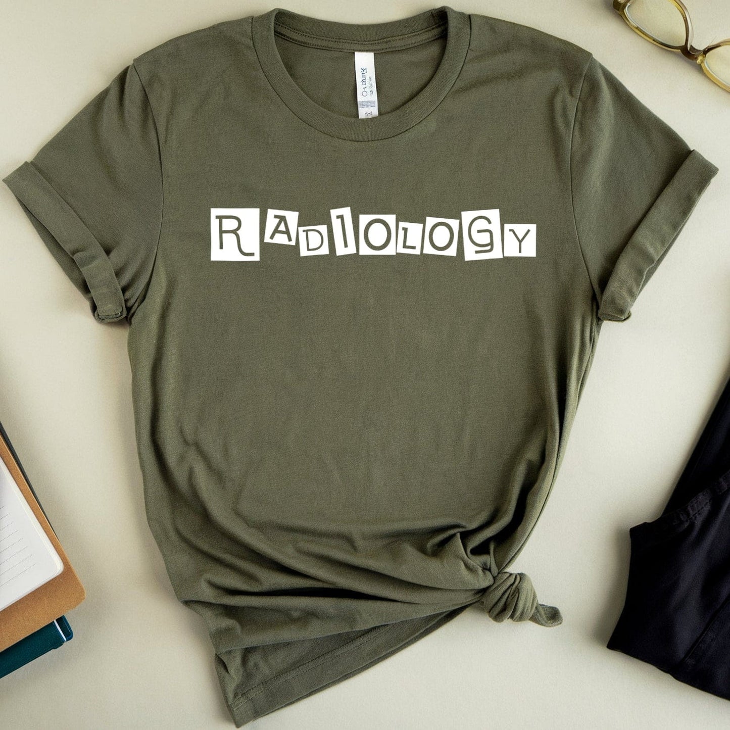 Green t-shirt with 'Radiology' text on a light surface with glasses and books.