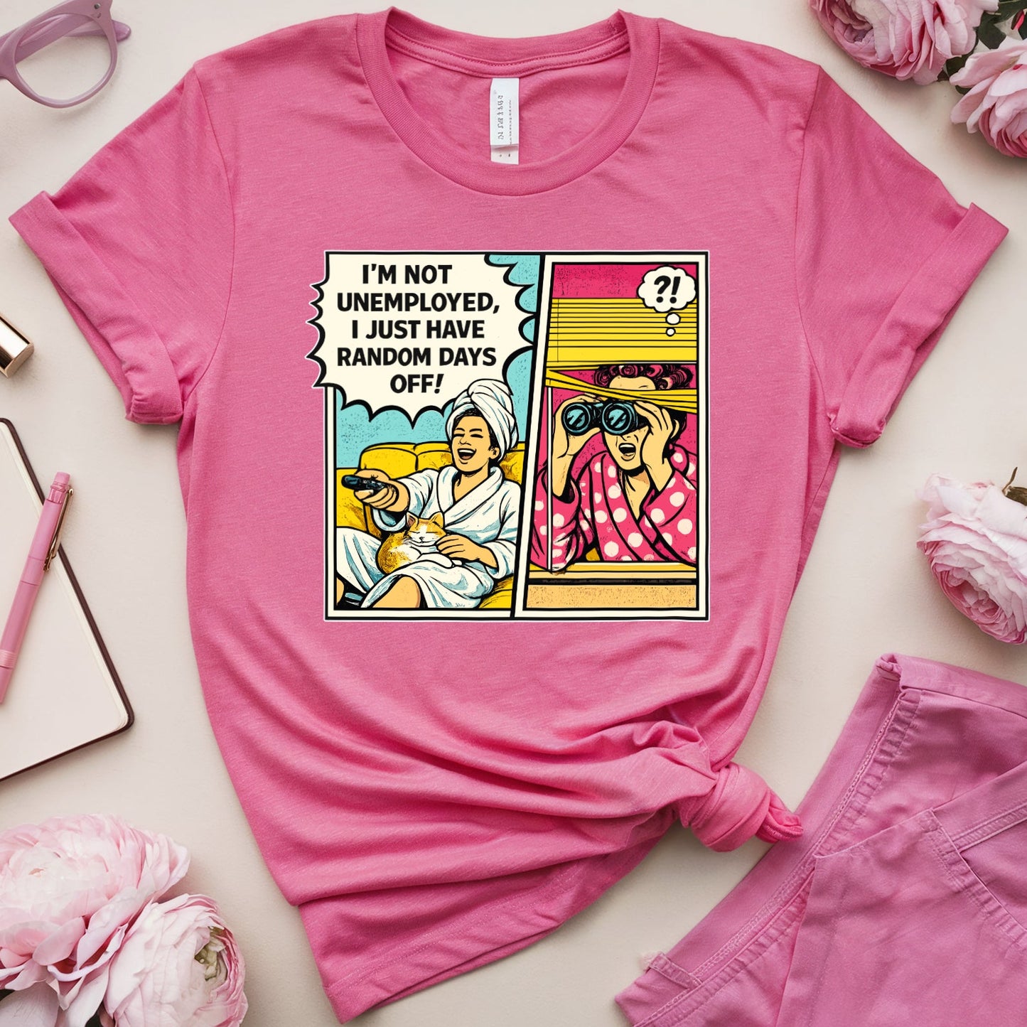 Pink t-shirt with comic design on a light surface with pink accessories and flowers.