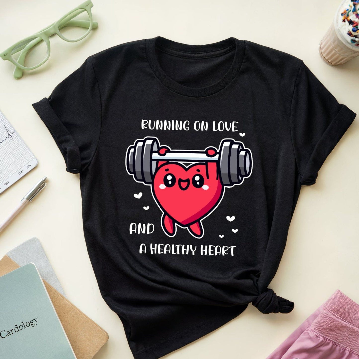 Black t-shirt with a heart and dumbbell graphic and text on a light surface with accessories.