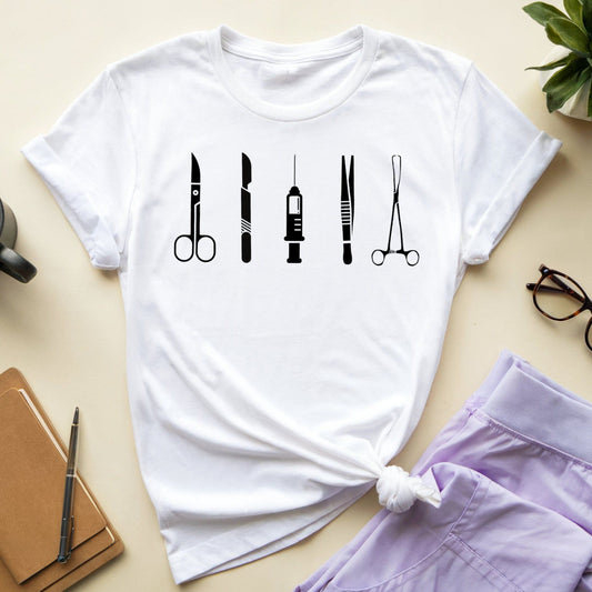 White t-shirt with black medical icon design on a beige surface with a cup, notebook, and glasses.