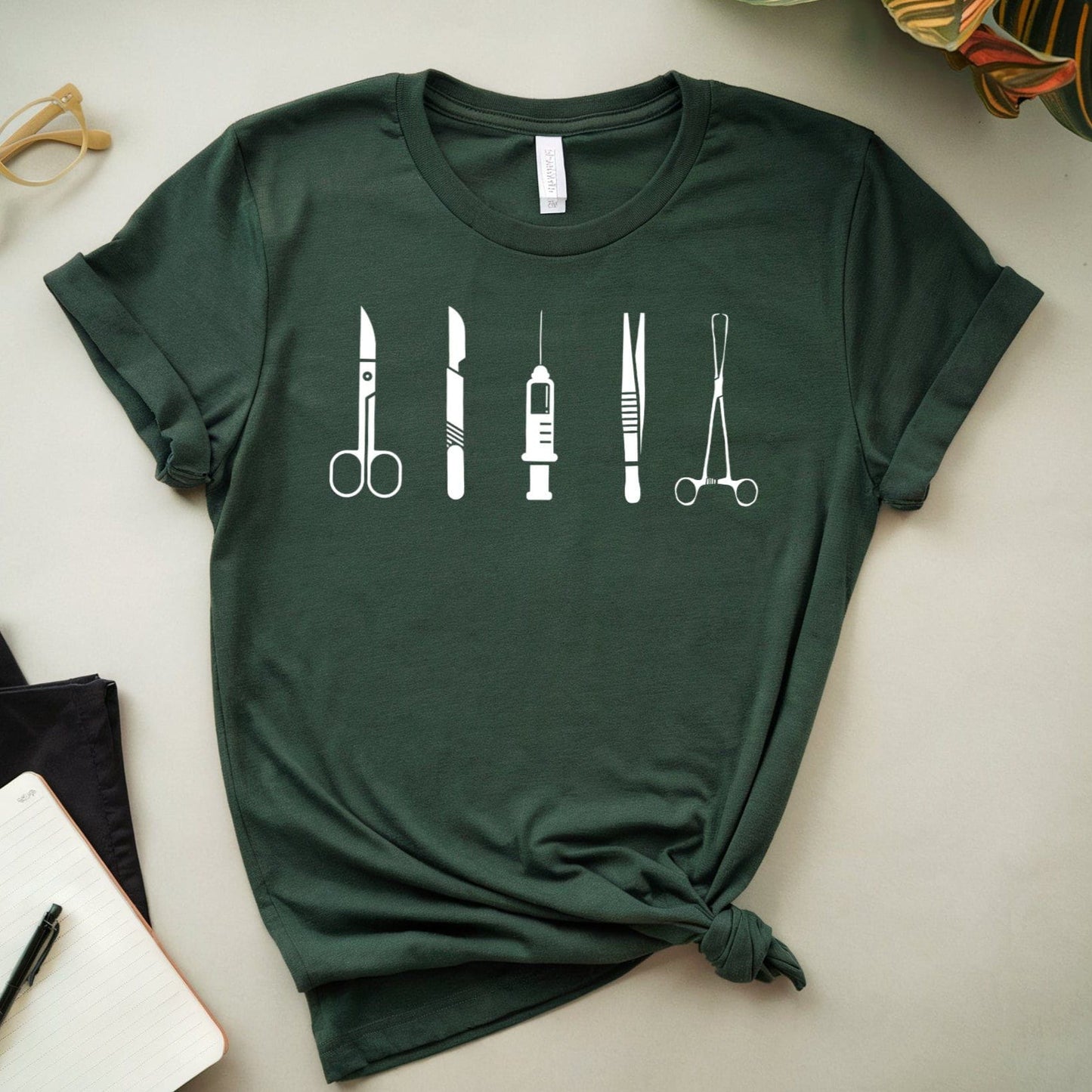 Green t-shirt with medical tool design on a light surface with glasses and notebook.