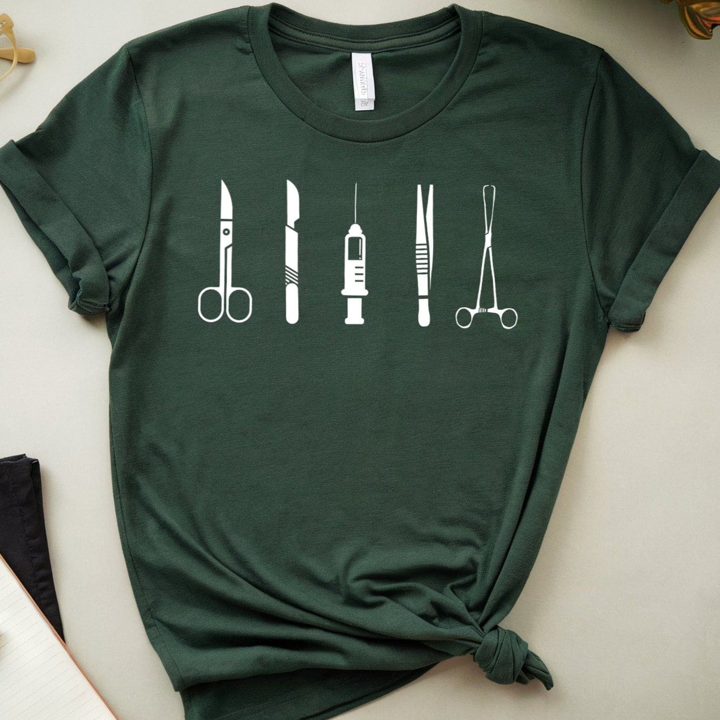 Green t-shirt with medical tool design on a light surface with glasses and notebook.