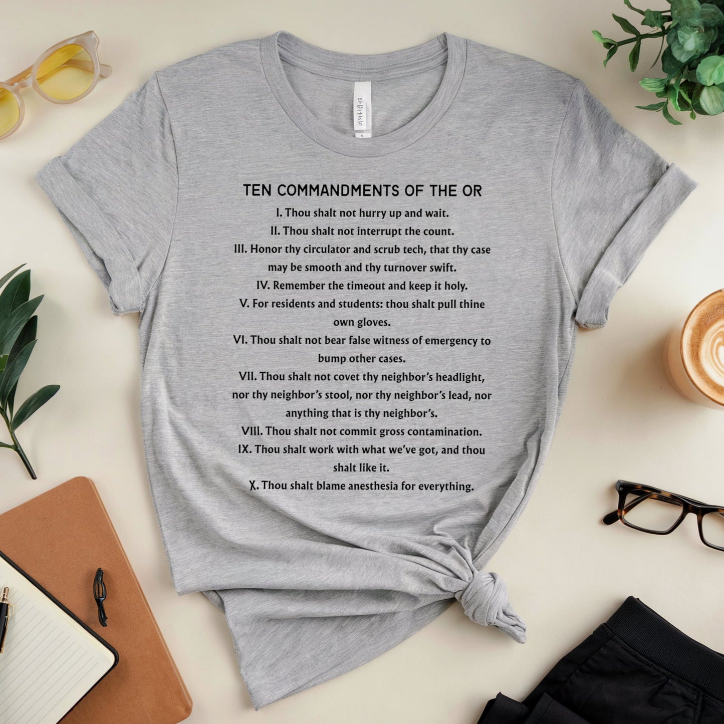 Gray t-shirt with 'Ten Commandments of the OR' text on a desk with office supplies.