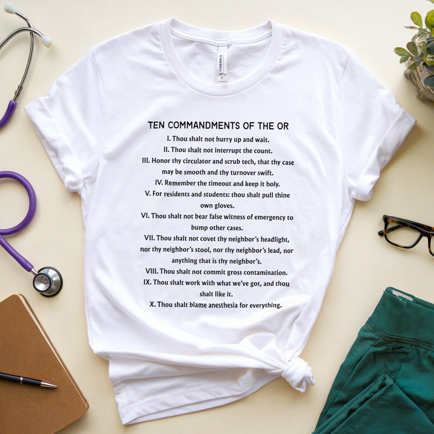 White t-shirt with 'Ten Commandments of the OR' text on a light surface with medical supplies.