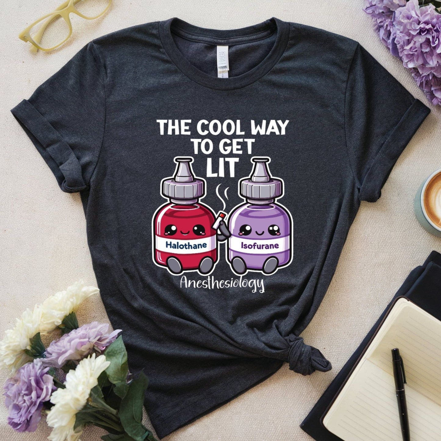 Grey t-shirt with graphic design and text on a light surface with flowers and a cup.