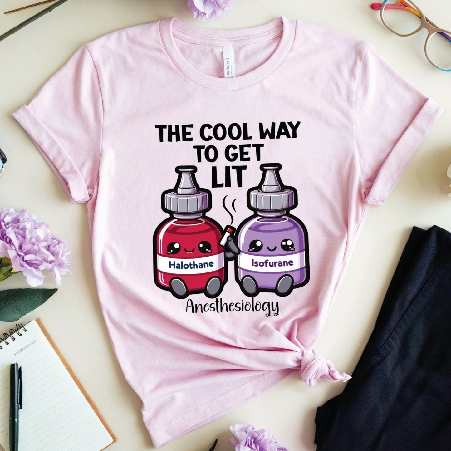 Pink t-shirt with anesthesiology-themed design on a light surface with flowers and glasses.