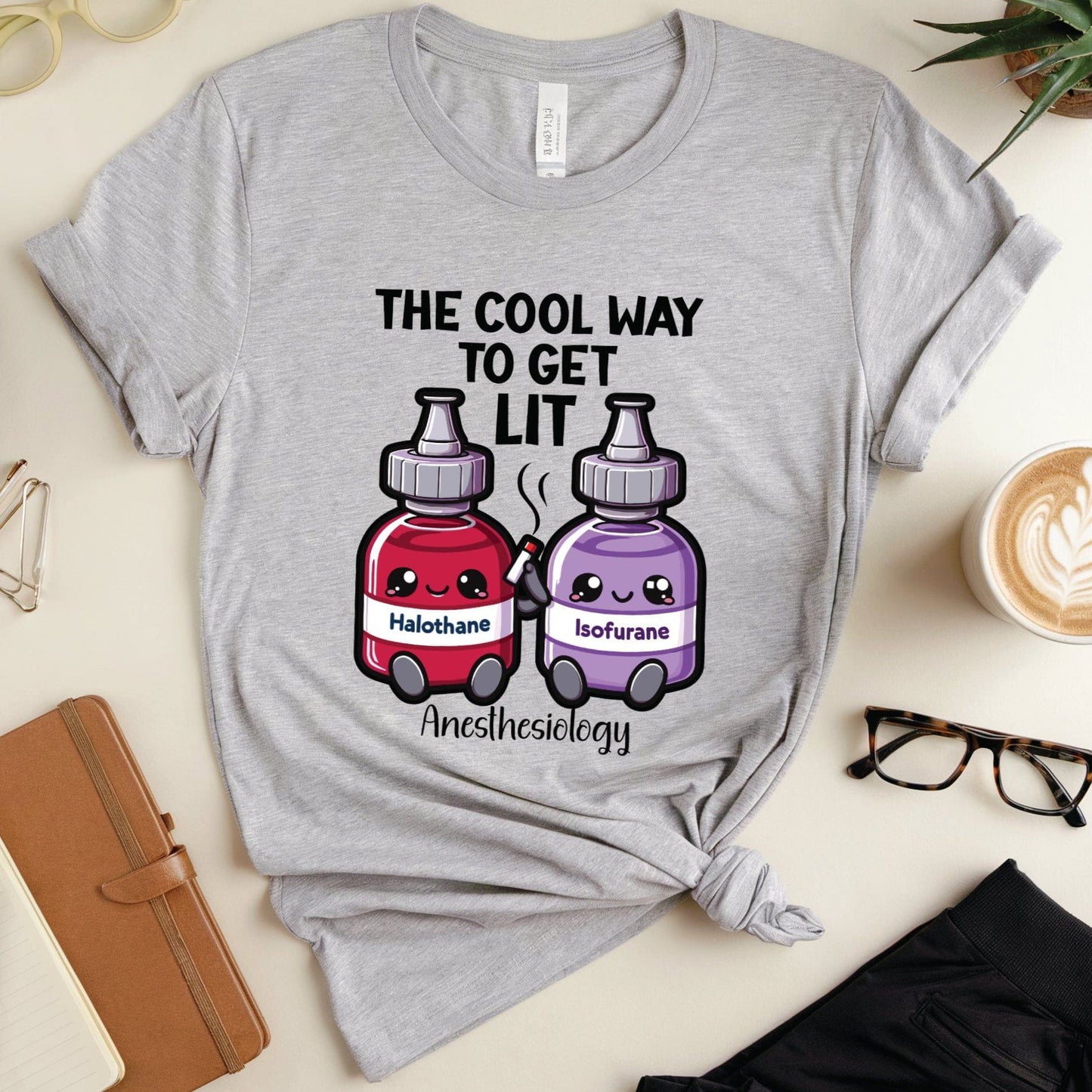 Gray t-shirt with anesthesiology-themed design on a table with stationery items.