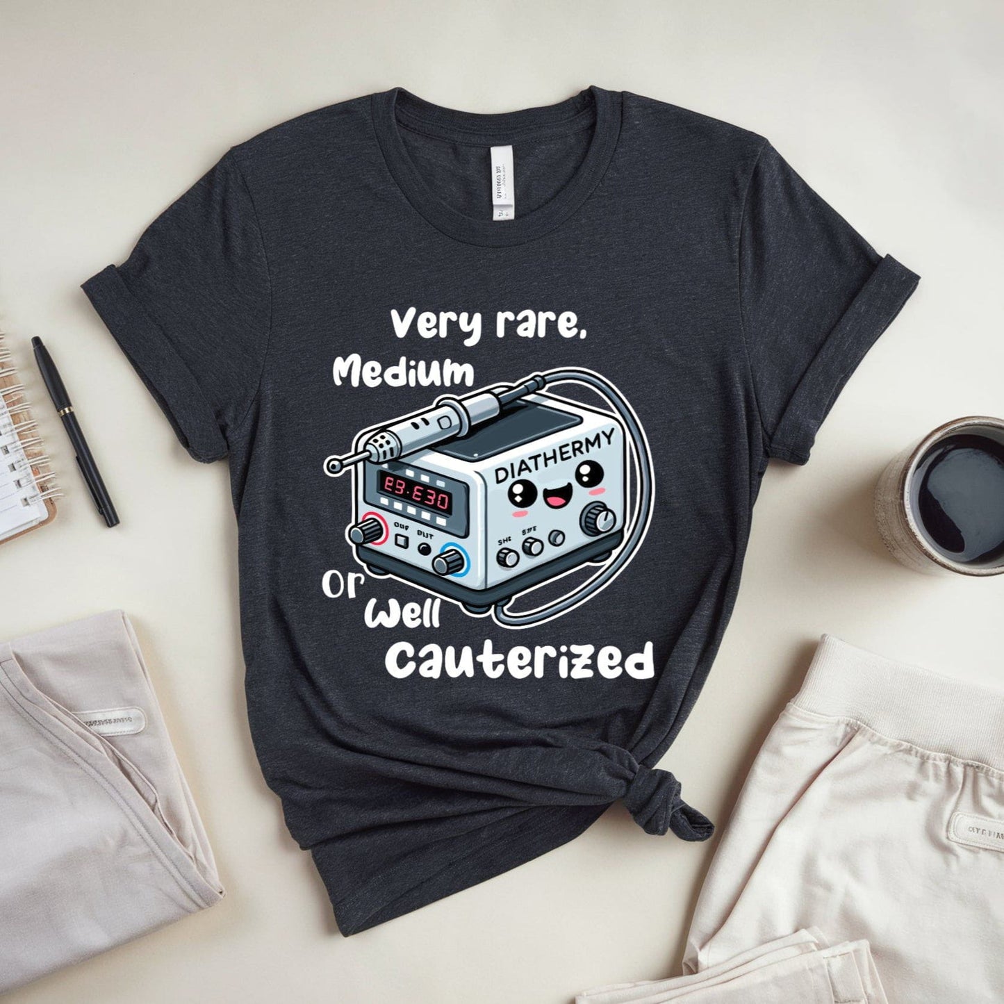 heather grey funny t-shirt for surgeons with medical device graphic and text on a light surface with casual items.