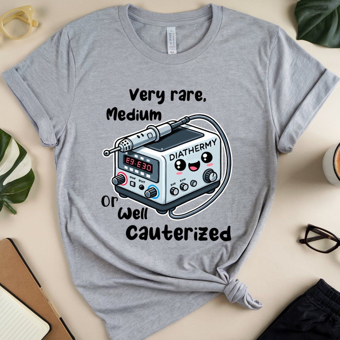 Gray t-shirt for surgeons with a graphic design on a beige surface with accessories.