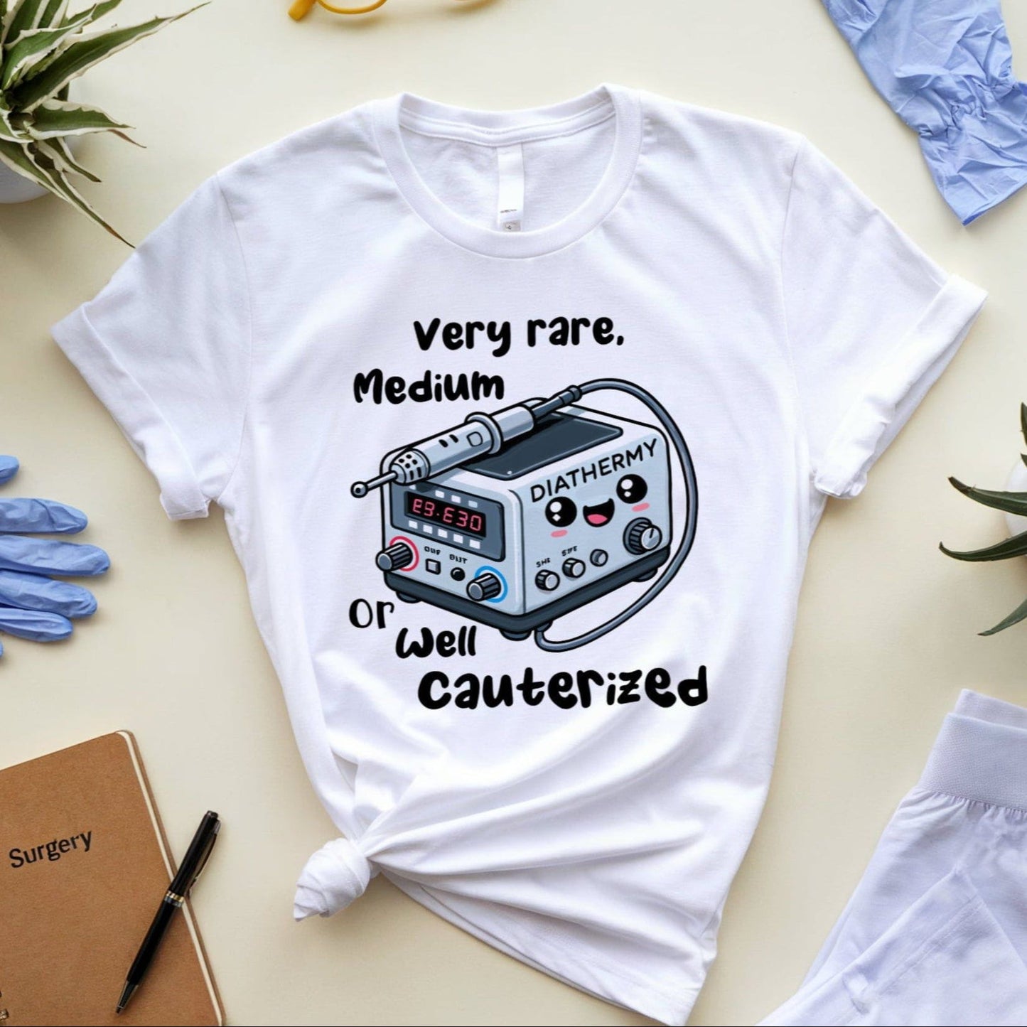 White t-shirt for surgeons with medical device graphic and text on a light surface with gloves and plants.