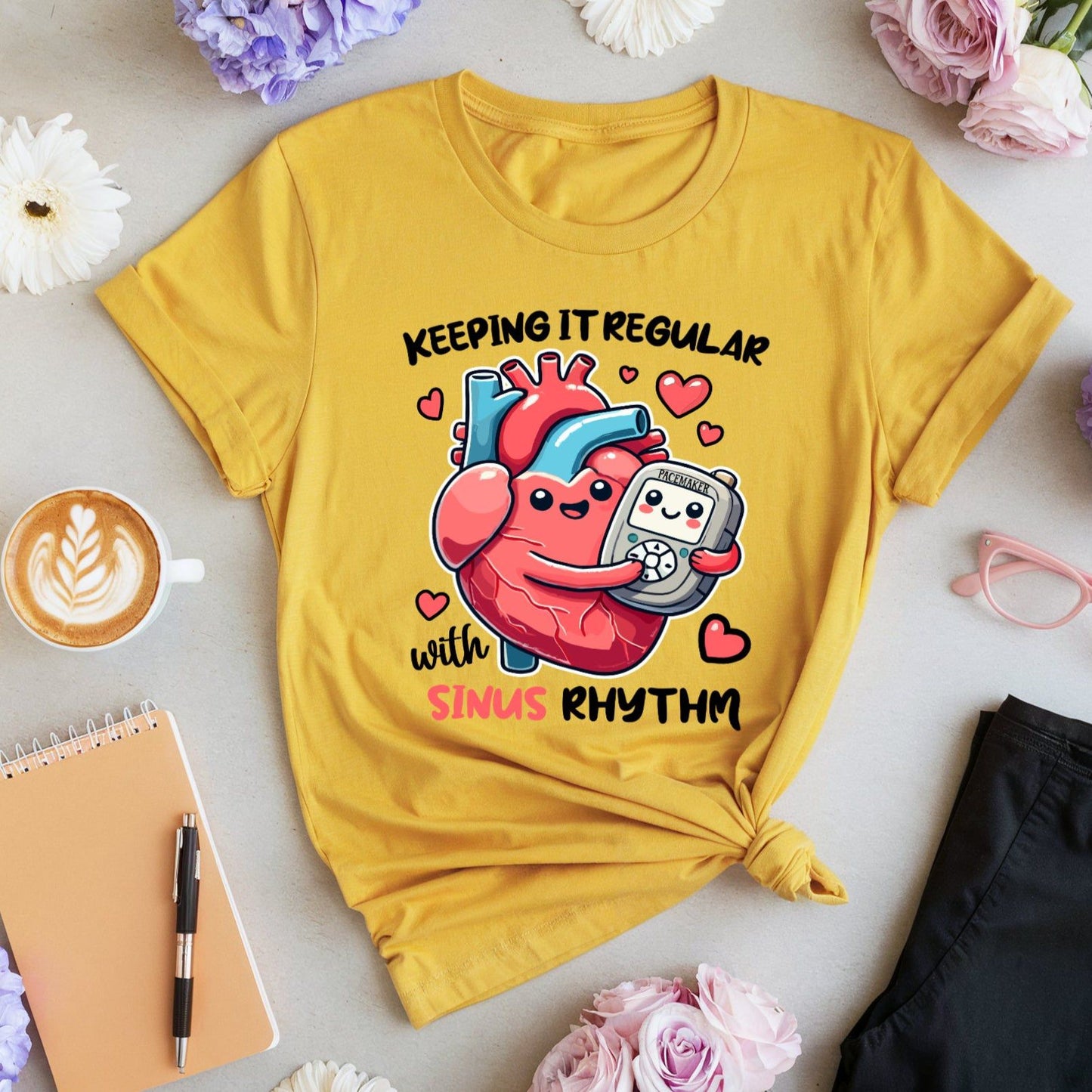 Yellow t-shirt for cardiologists with heart and pacemaker graphic and text, surrounded by flowers and a cup of coffee.