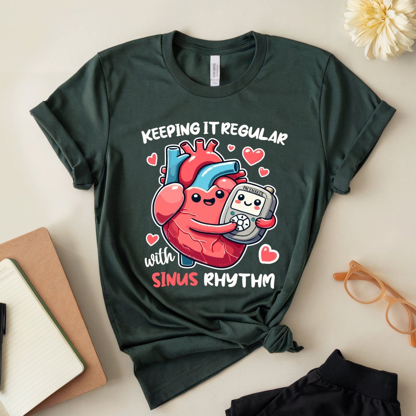 Green t-shirt for cardiology with heart and pacemaker graphic and text on a light surface with accessories.