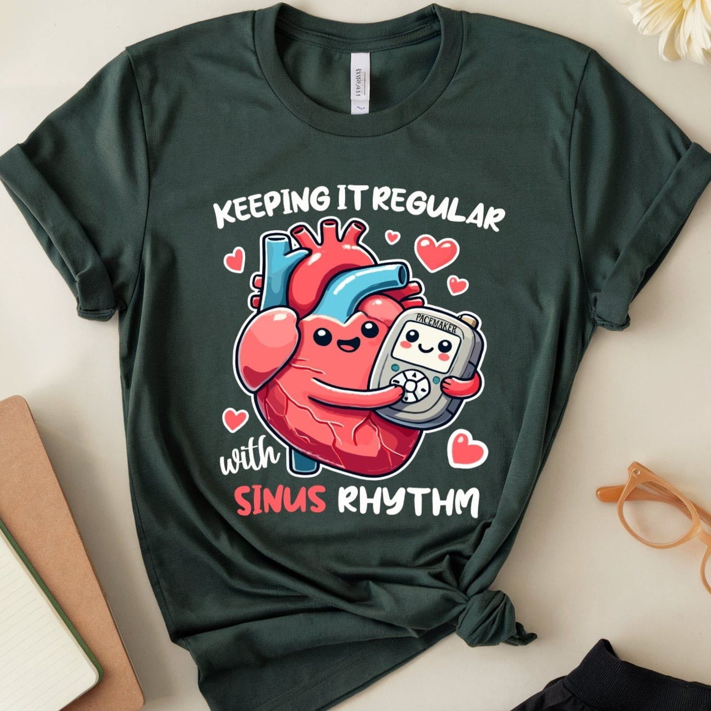 Green t-shirt for cardiology with heart and pacemaker graphic and text on a light surface with accessories.